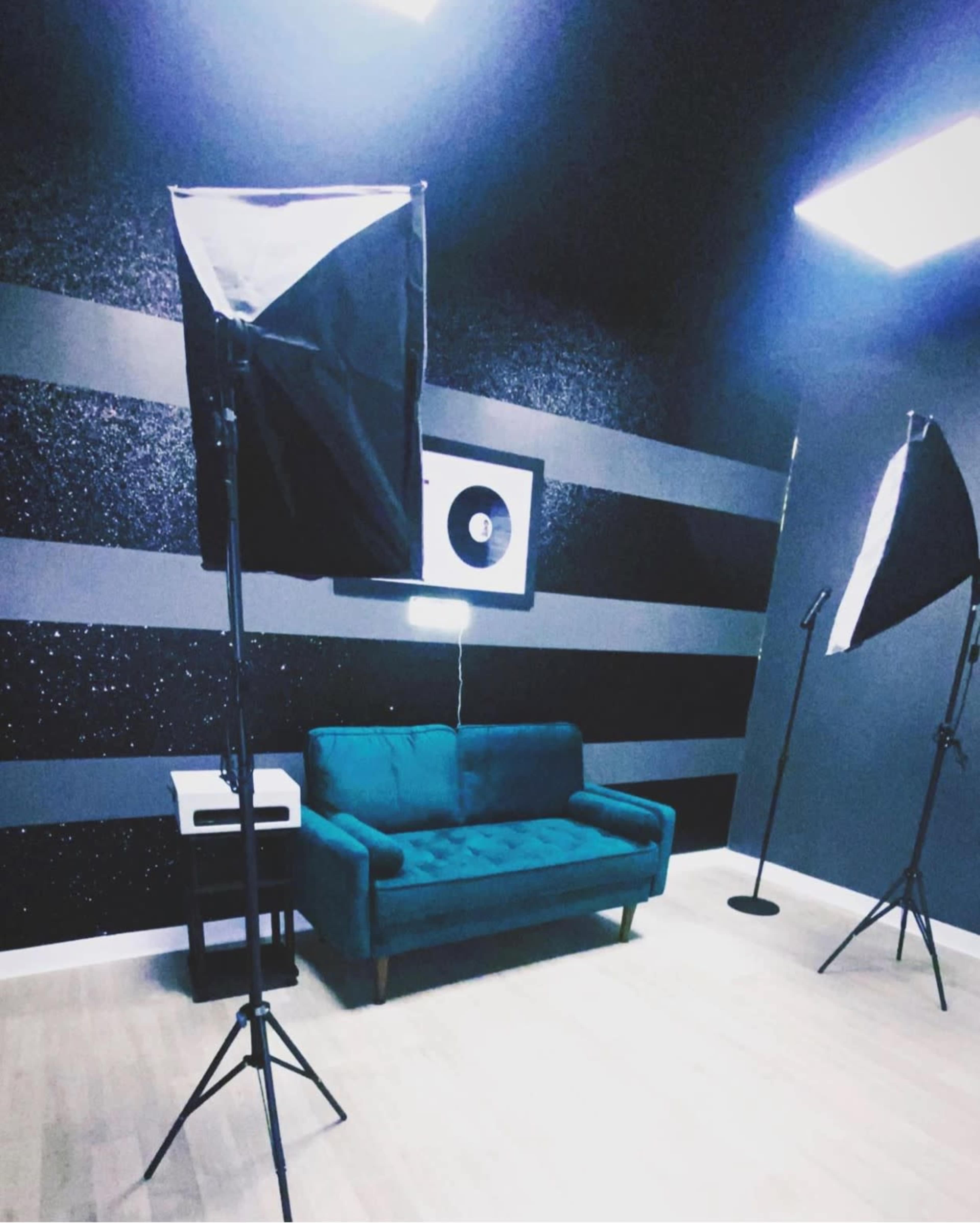 A photography studio with a teal couch, softbox lights, and a framed vinyl record on the wall.