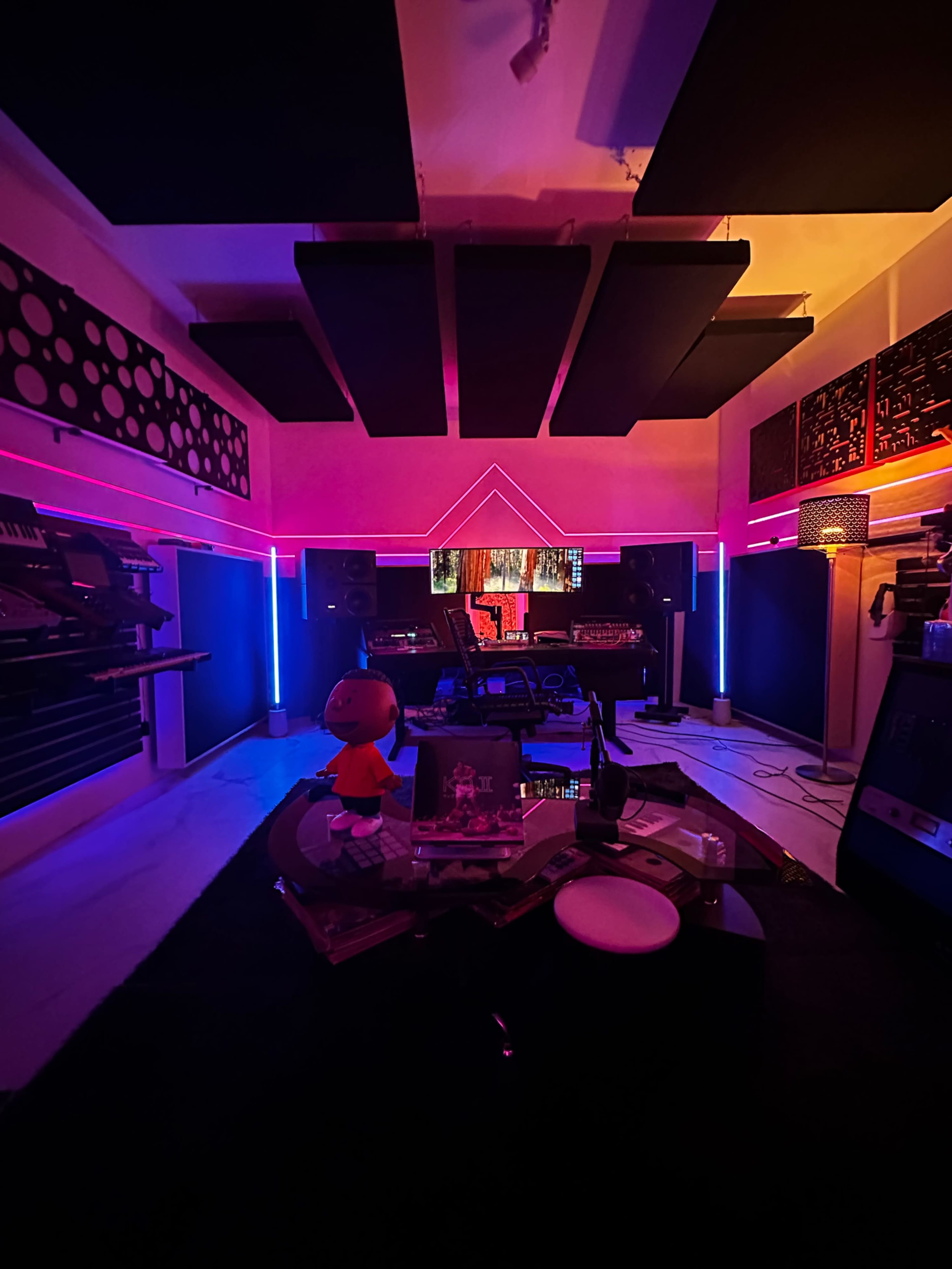 The image shows a modern music studio with colorful LED lighting, a range of musical equipment, and various vinyl records scattered on a table.