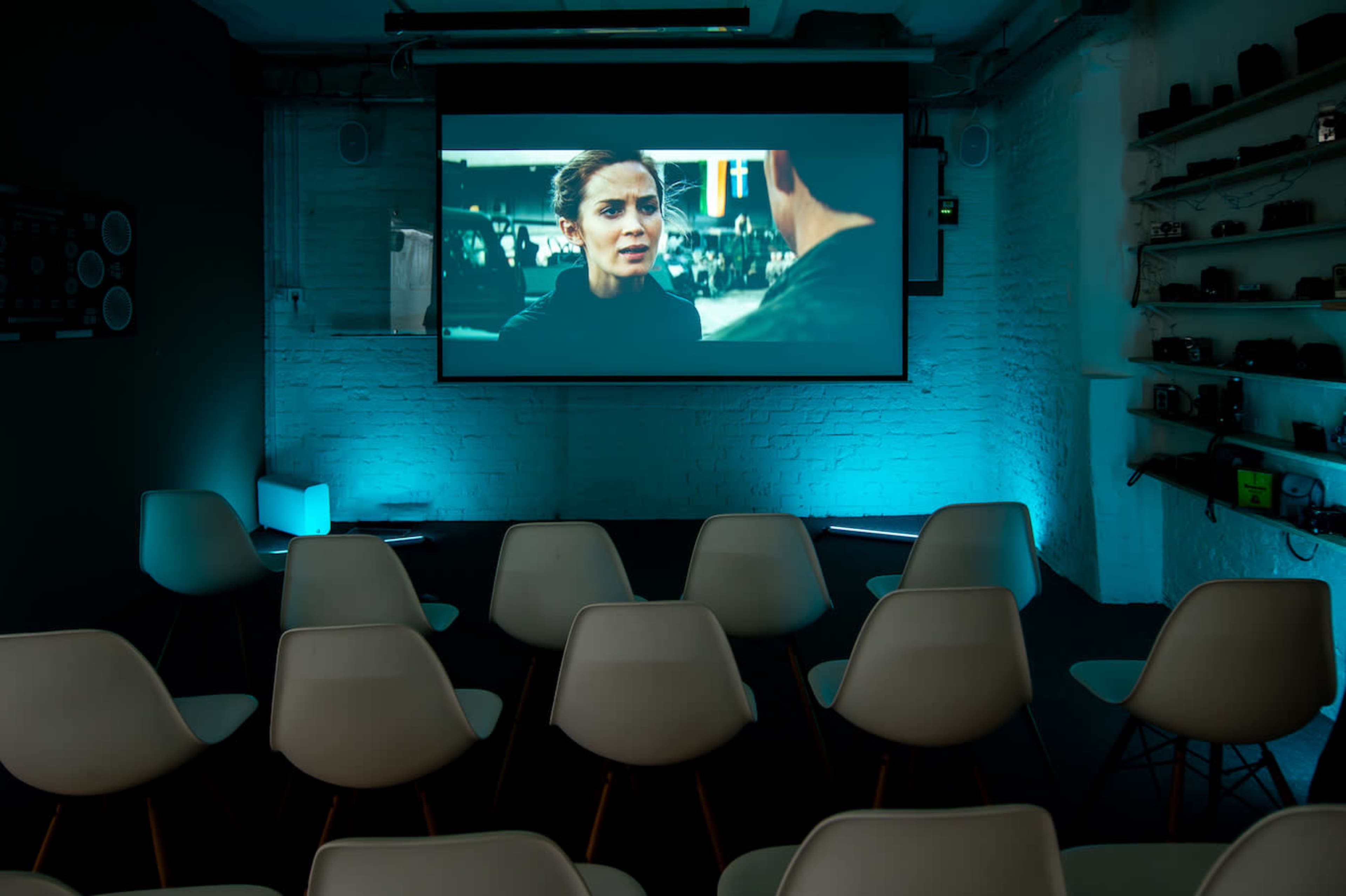 A movie screening room with rows of white chairs facing a large screen displaying a film scene.