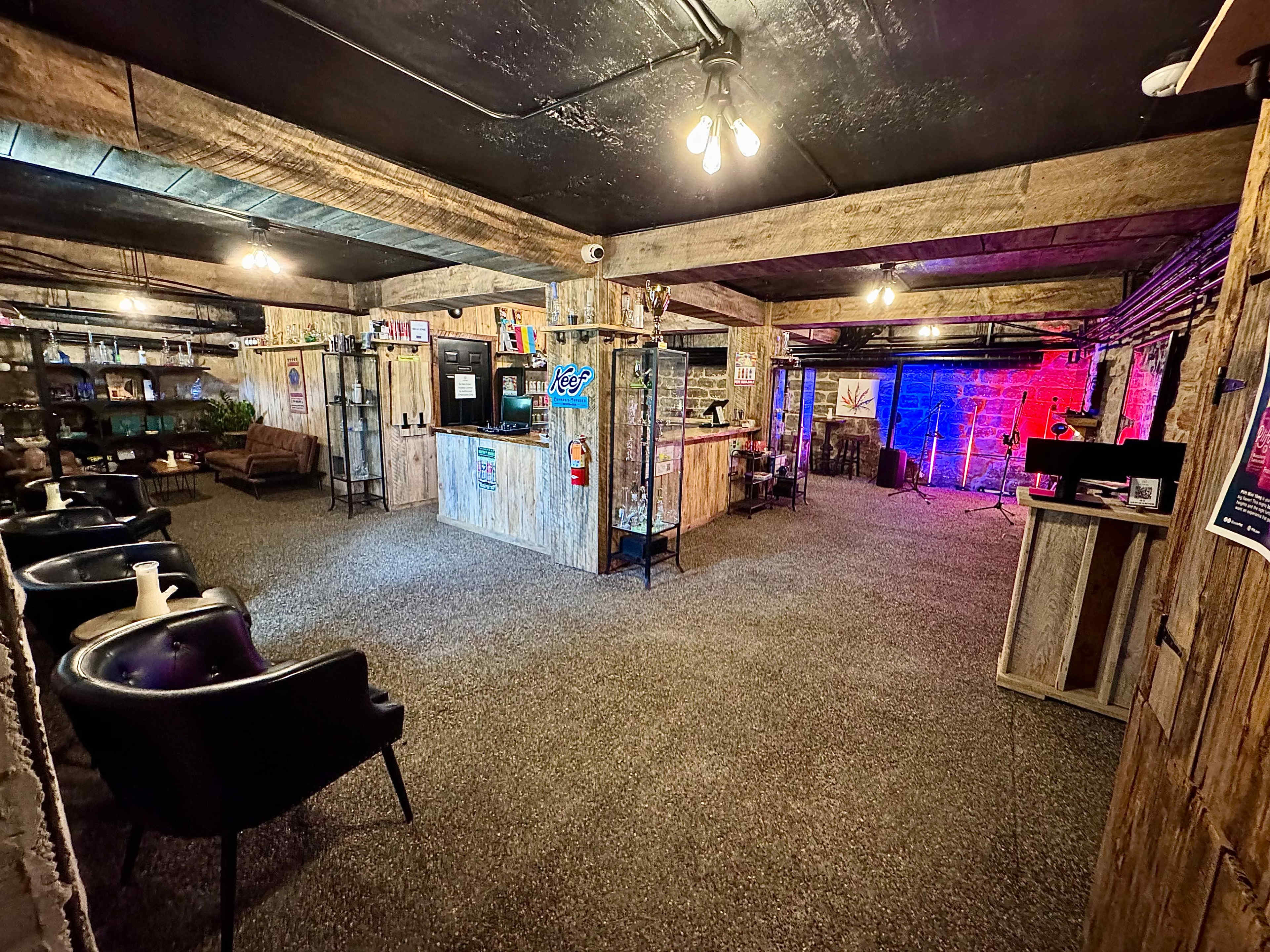 The image shows a spacious interior resembling a rustic lounge with wooden decor, a bar area, and soft seating against a backdrop of colorful lighting.