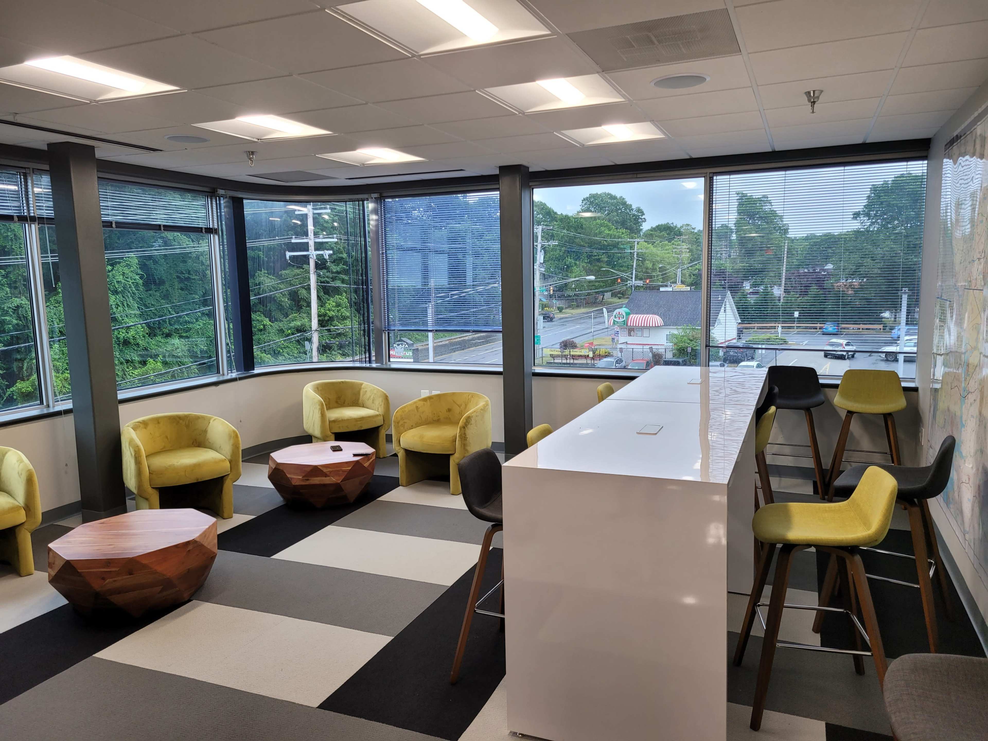A modern office space with curved windows, featuring yellow and gray chairs, wooden tables, and a white counter.