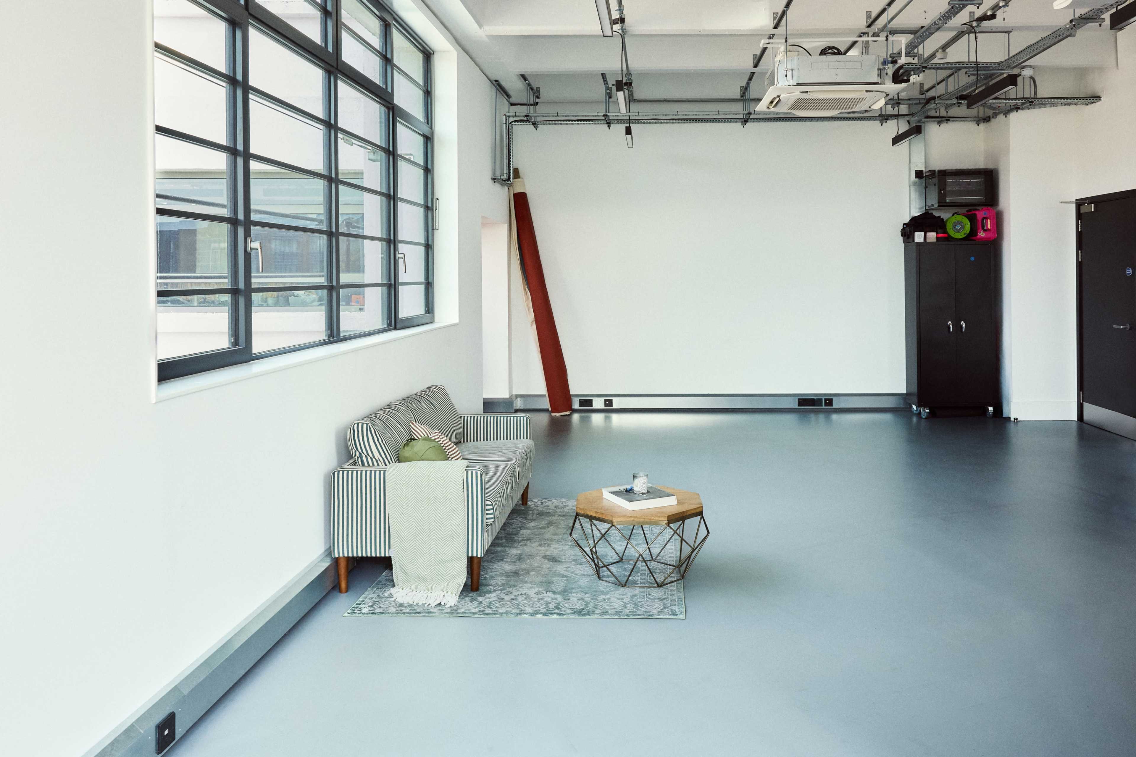 The image shows a minimalist interior space featuring a striped couch, a small coffee table with a geometric base, and large windows allowing natural light.