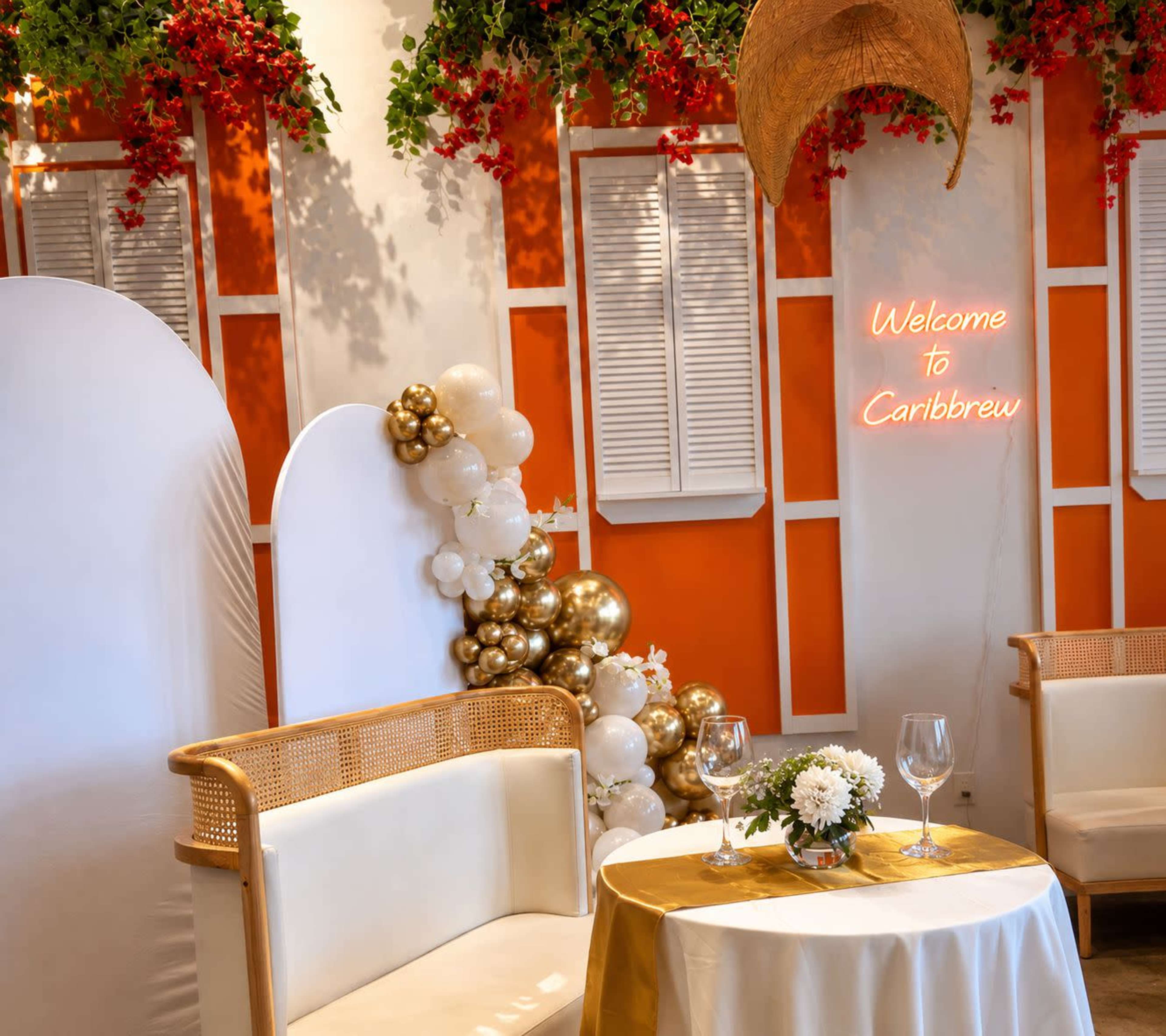 The scene features a decorated indoor space with white furnishings, floral arrangements, and a neon sign that reads "Welcome to Caribbrew."
