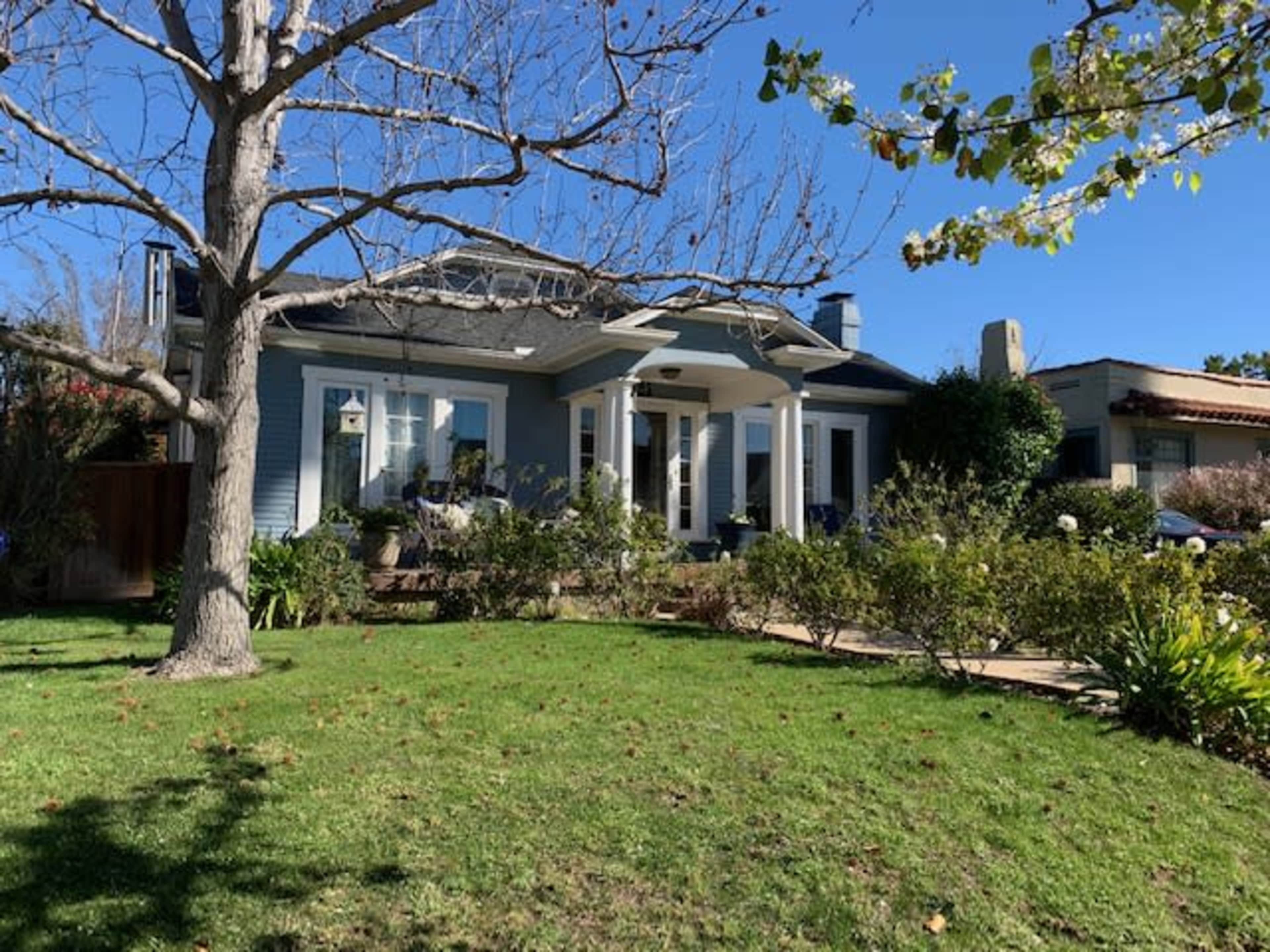 A light blue house with white columns and a landscaped front yard is visible under a clear blue sky.