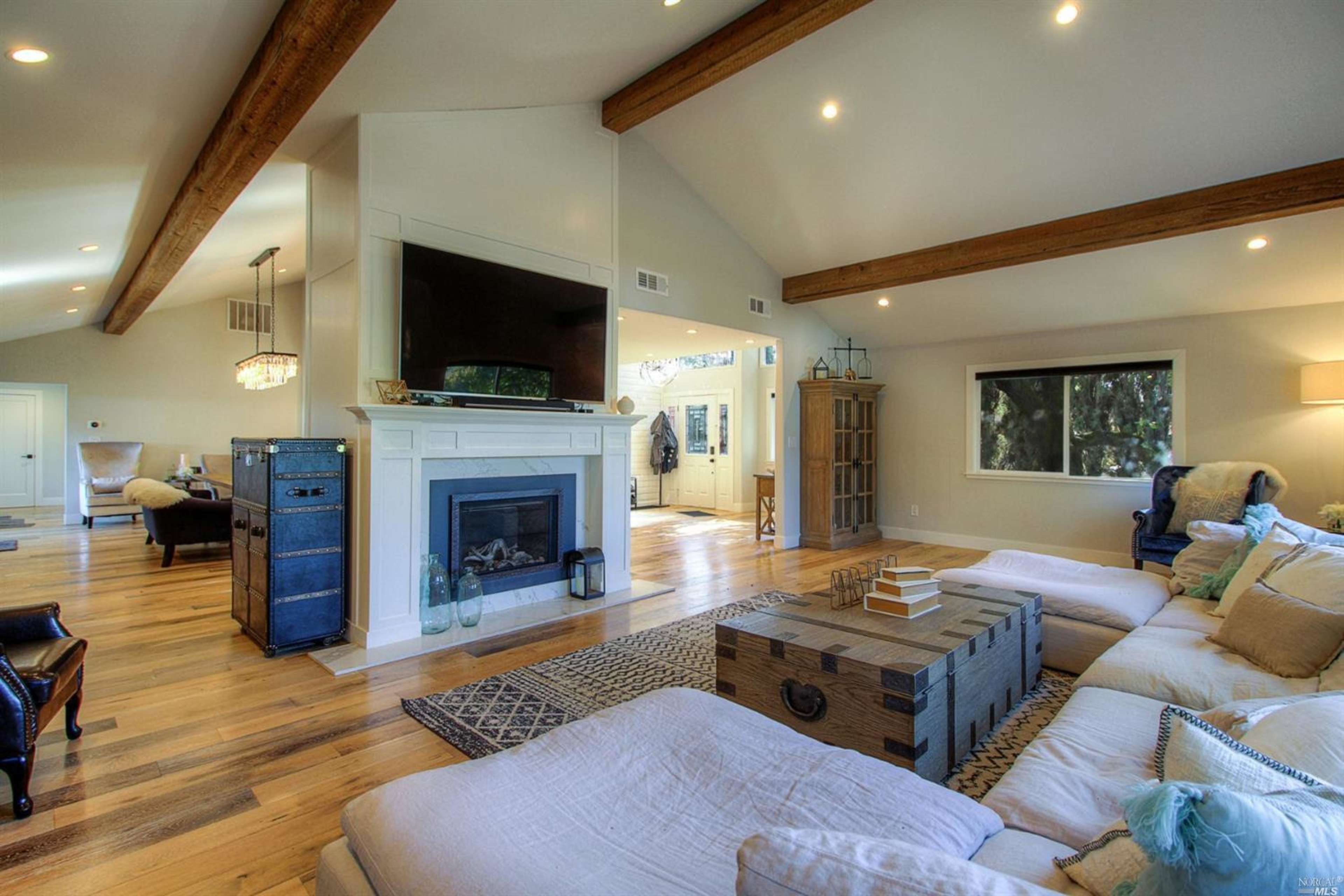 A spacious living room featuring a large sectional sofa, a fireplace with a modern mantel, and wooden beams on the ceiling.