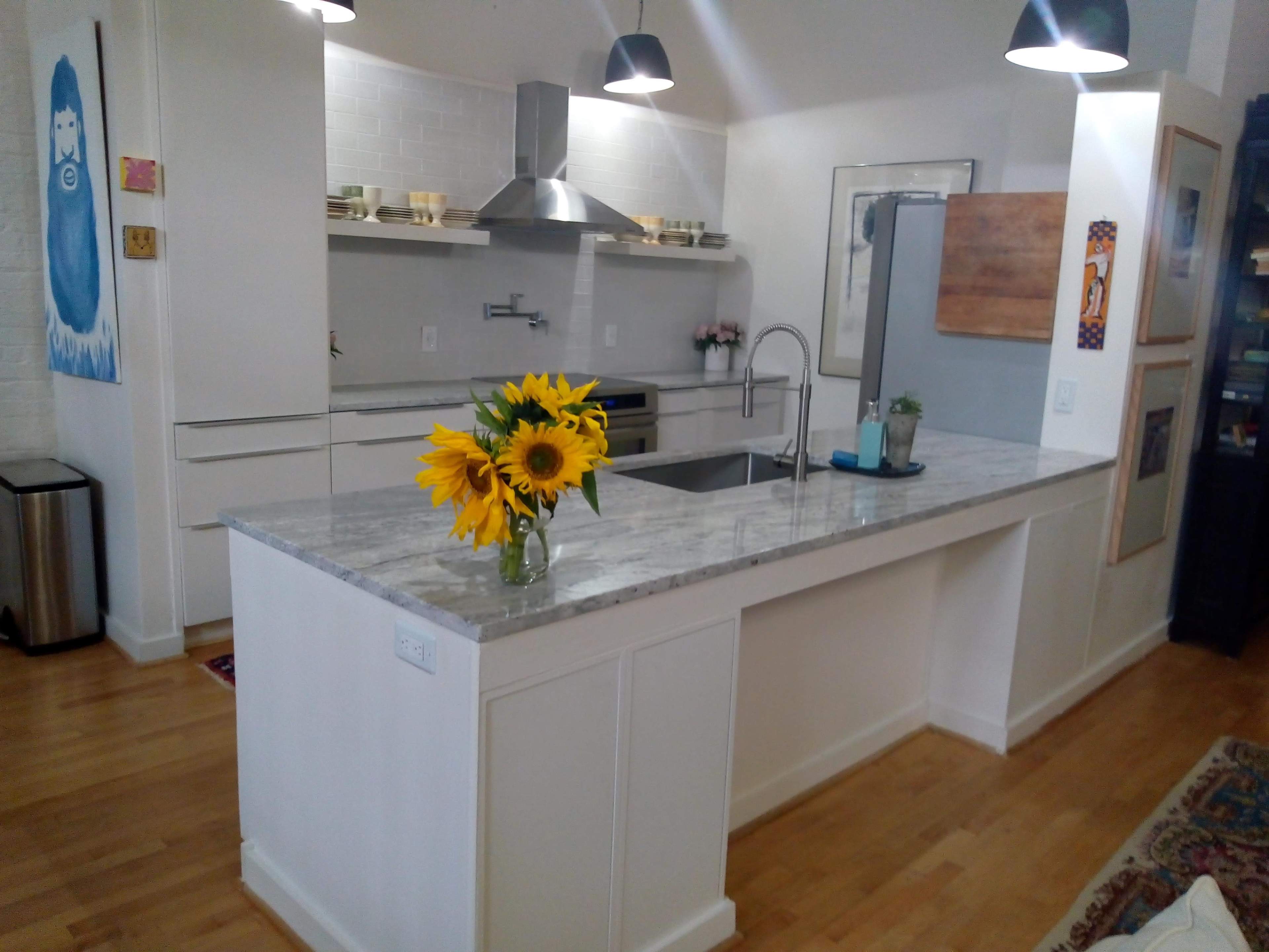 A modern kitchen with a marble countertop, stainless steel appliances, and a vase of sunflowers on the island.