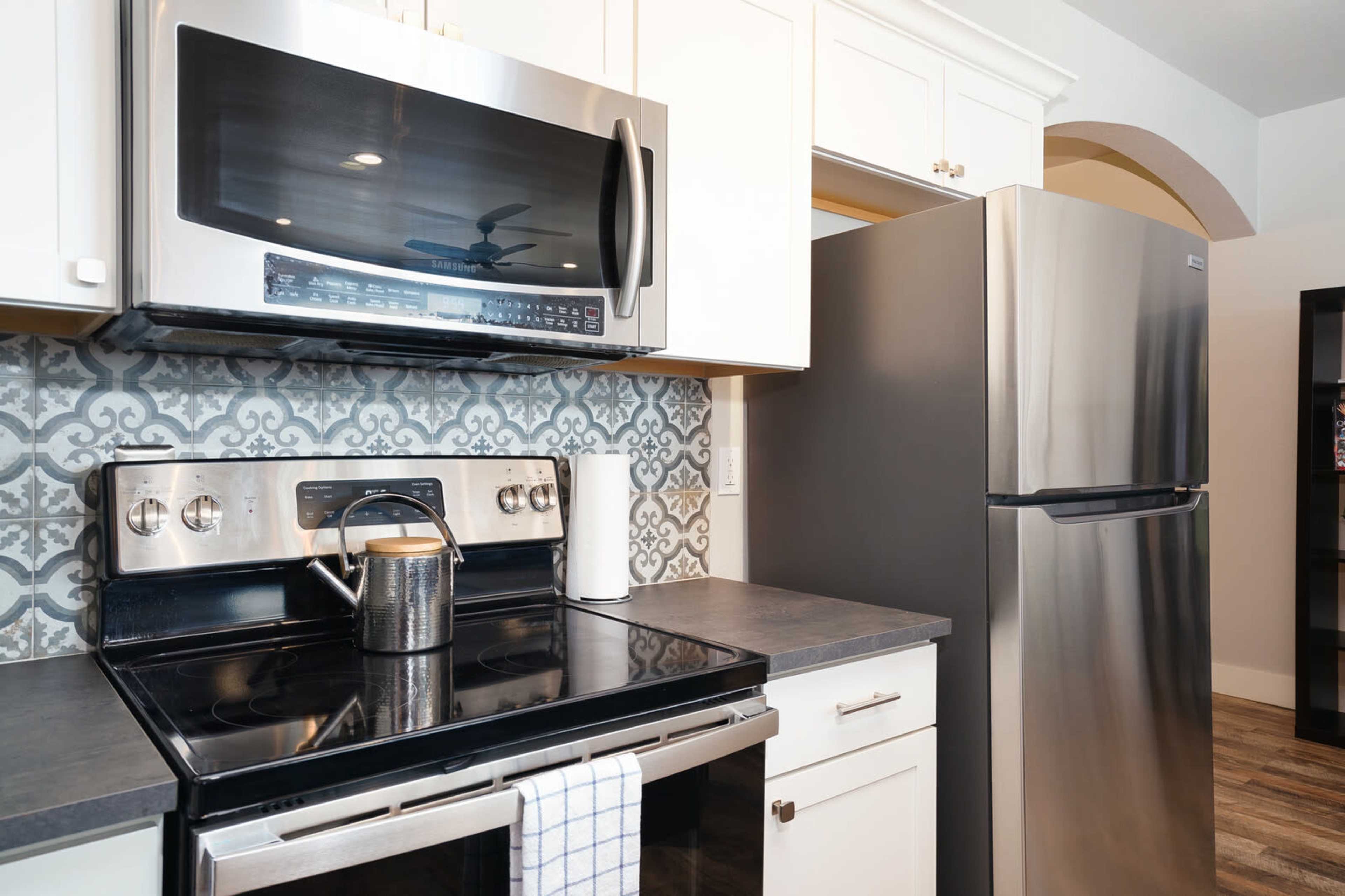 A modern kitchen with stainless steel appliances, including a microwave, stovetop, and refrigerator, set against a patterned backsplash.