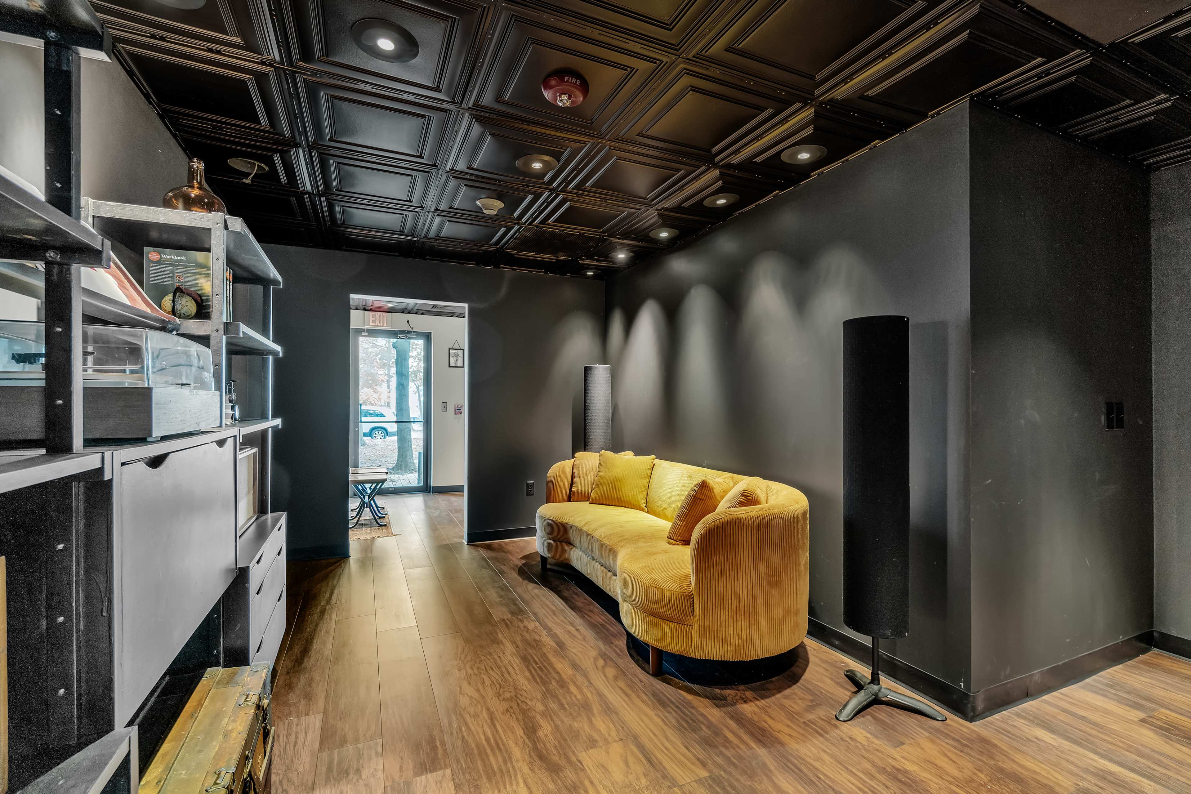 The image shows a modern room featuring a curved yellow sofa, dark walls, and a black ceiling with recessed lighting.