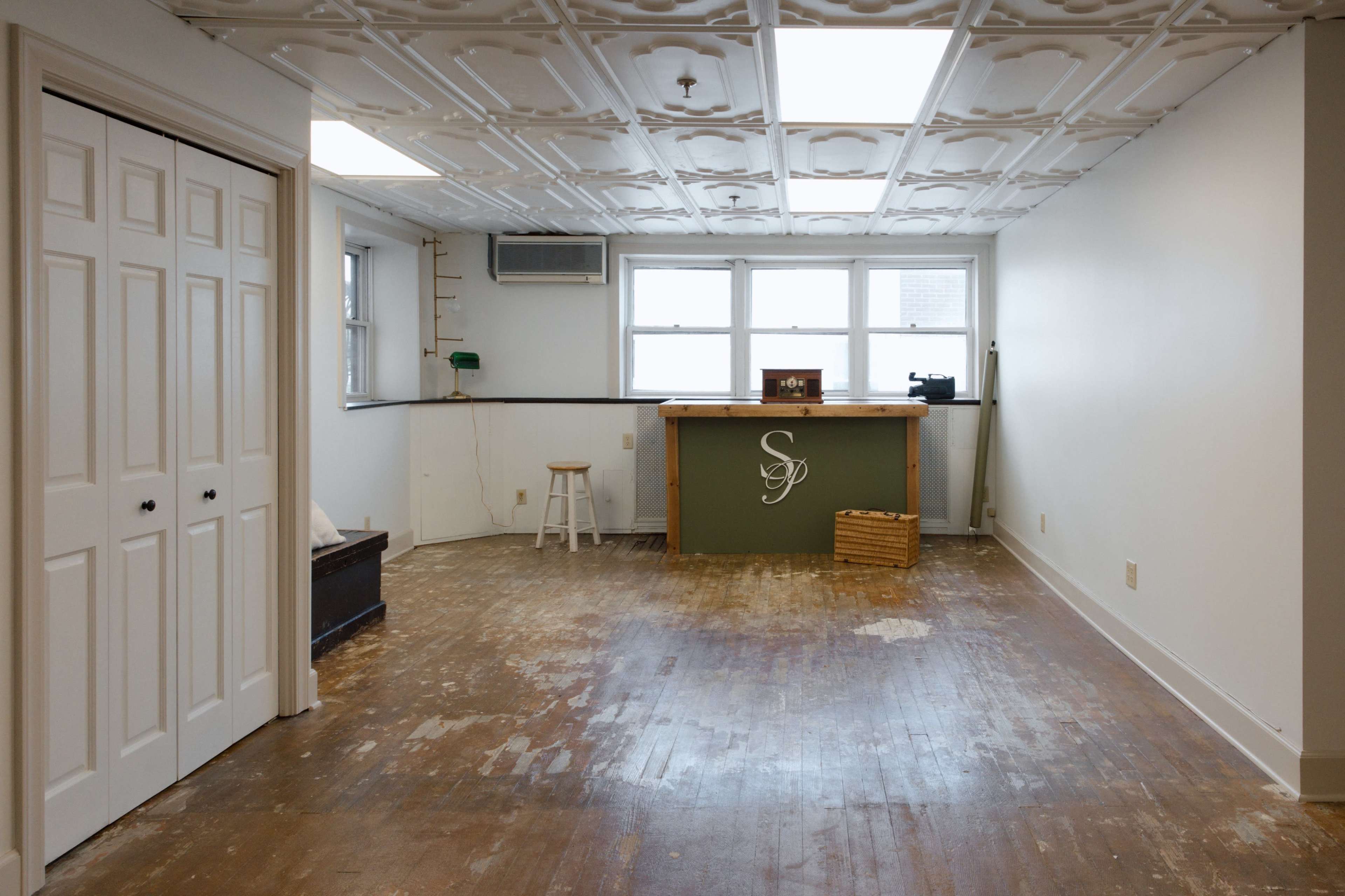 The image shows an empty room with a wooden floor, a bar area on one side, and a closet on the opposite side.