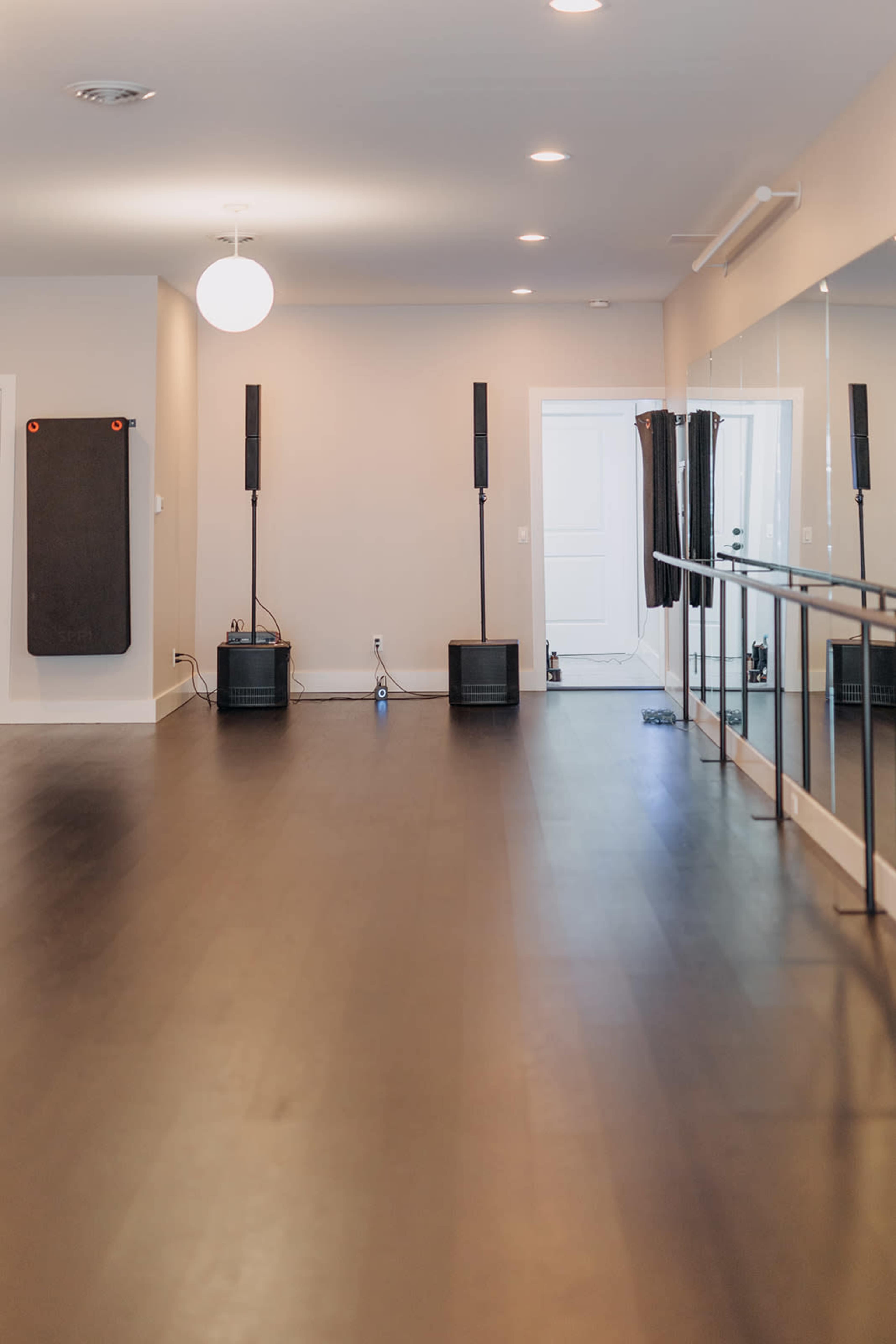 A spacious dance studio with black flooring, mirrored walls, and two speaker stands placed on opposite sides of the room.