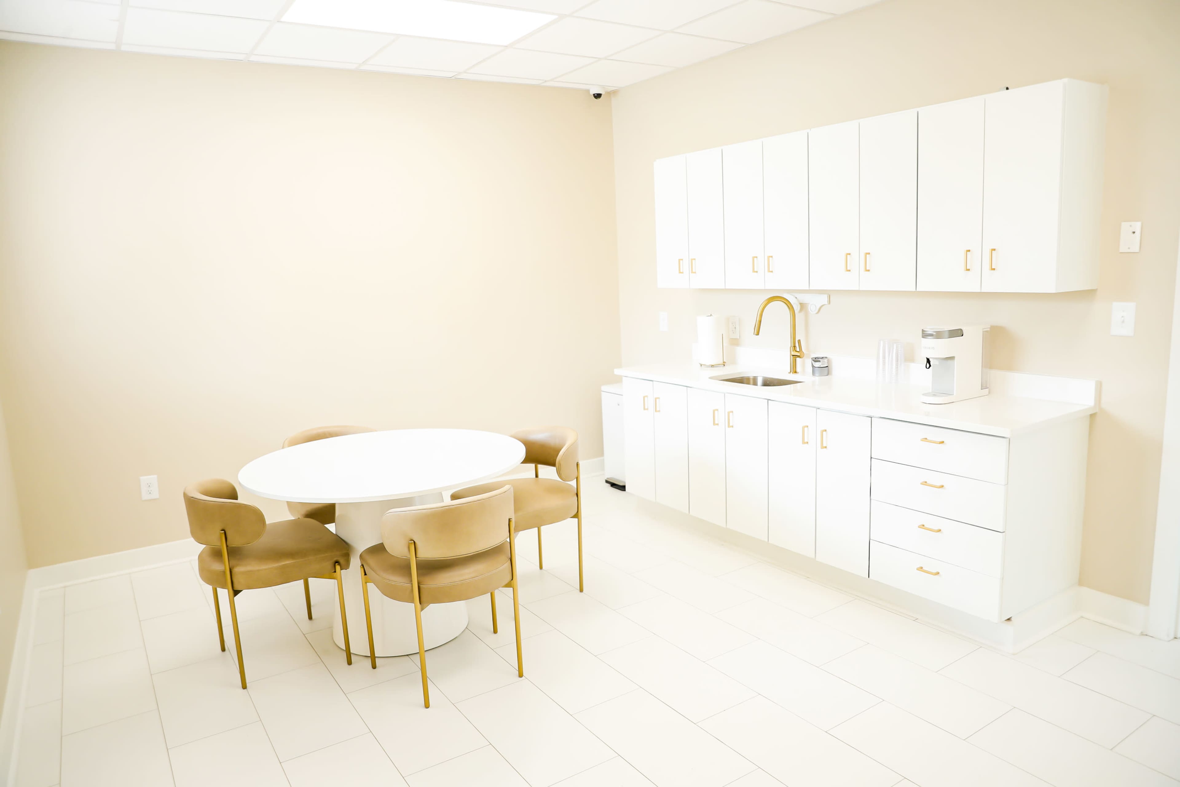 A bright, minimalist kitchen features a round table with four chairs and a cabinetry area equipped with appliances.