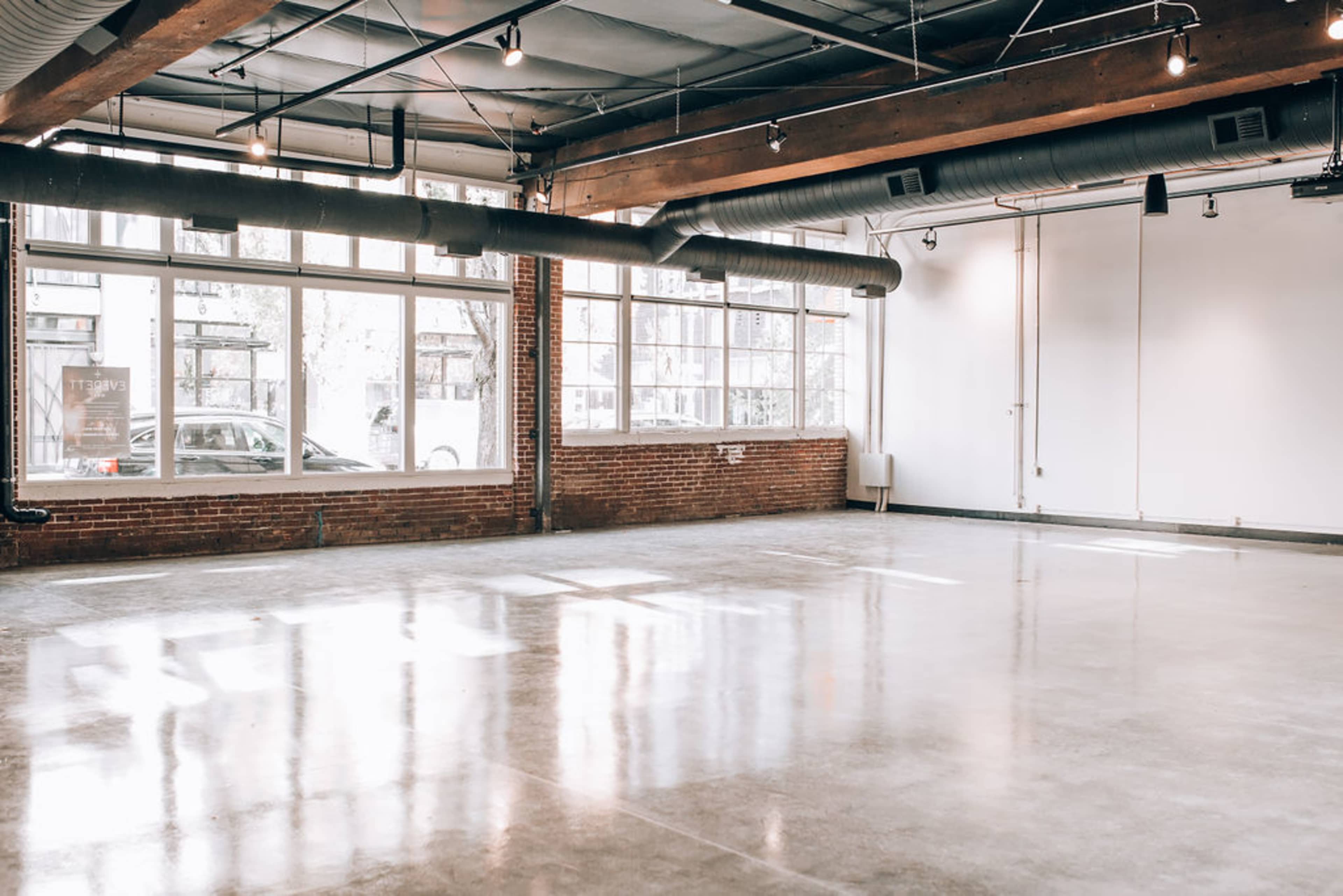 An empty, well-lit industrial space with large windows and polished concrete flooring.