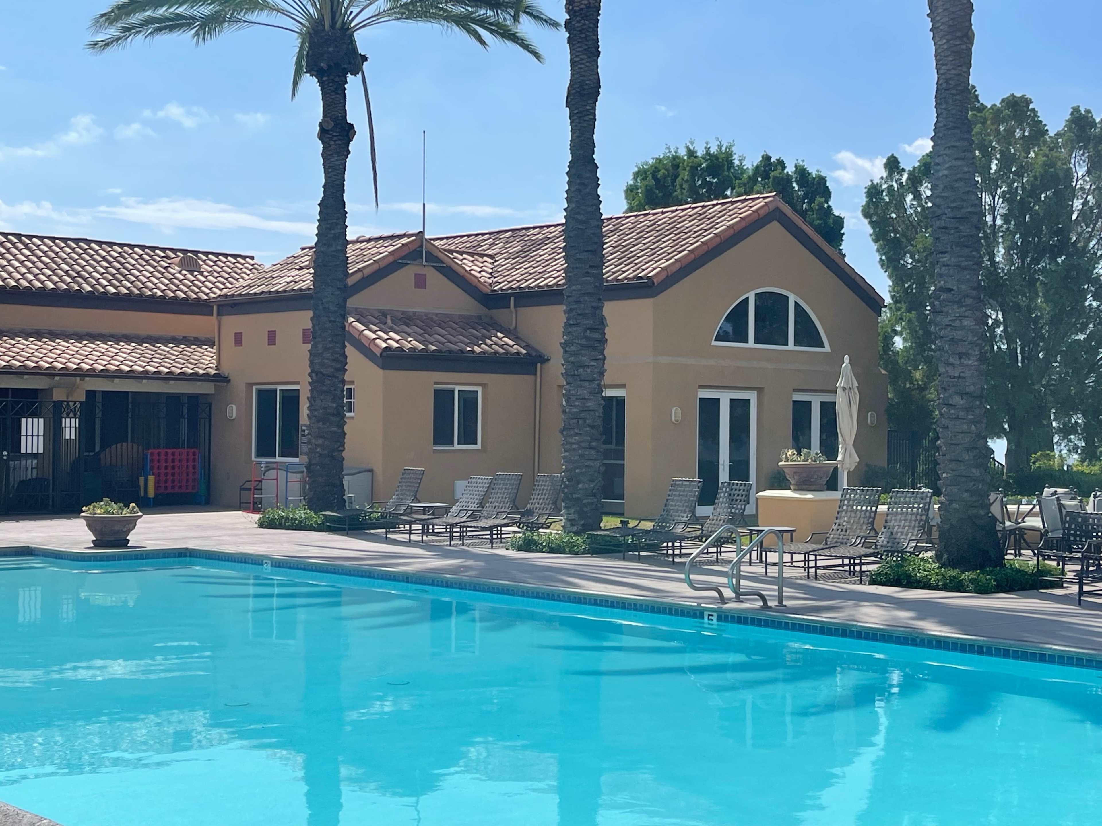A clear blue swimming pool reflecting a building with a tiled roof and palm trees in the background.