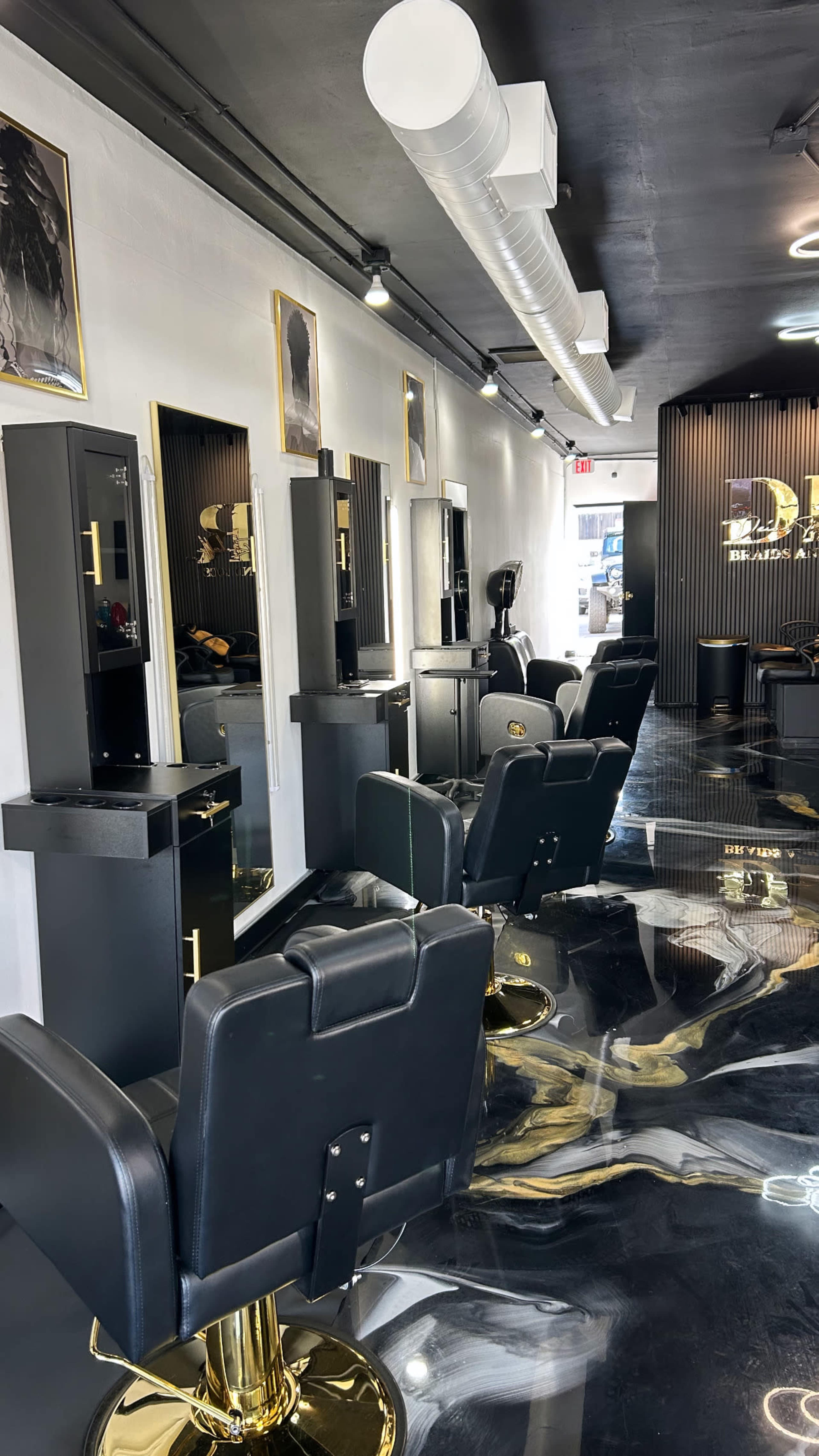 The image shows a modern barber shop interior with several black styling chairs, mirrored stations, and a sleek black and gold aesthetic.