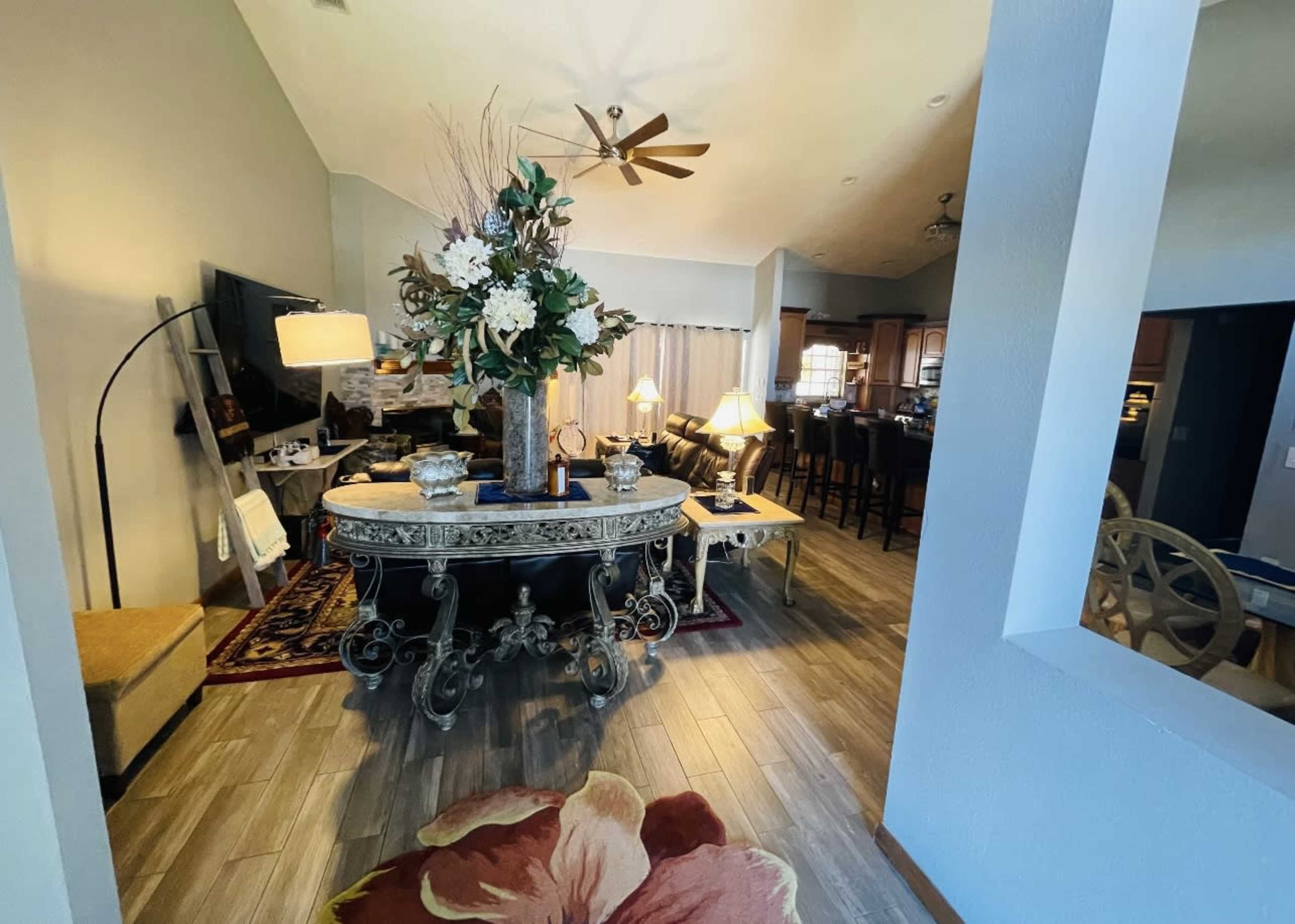A spacious living area with a decorative table, a large floral arrangement, and an open kitchen in the background.