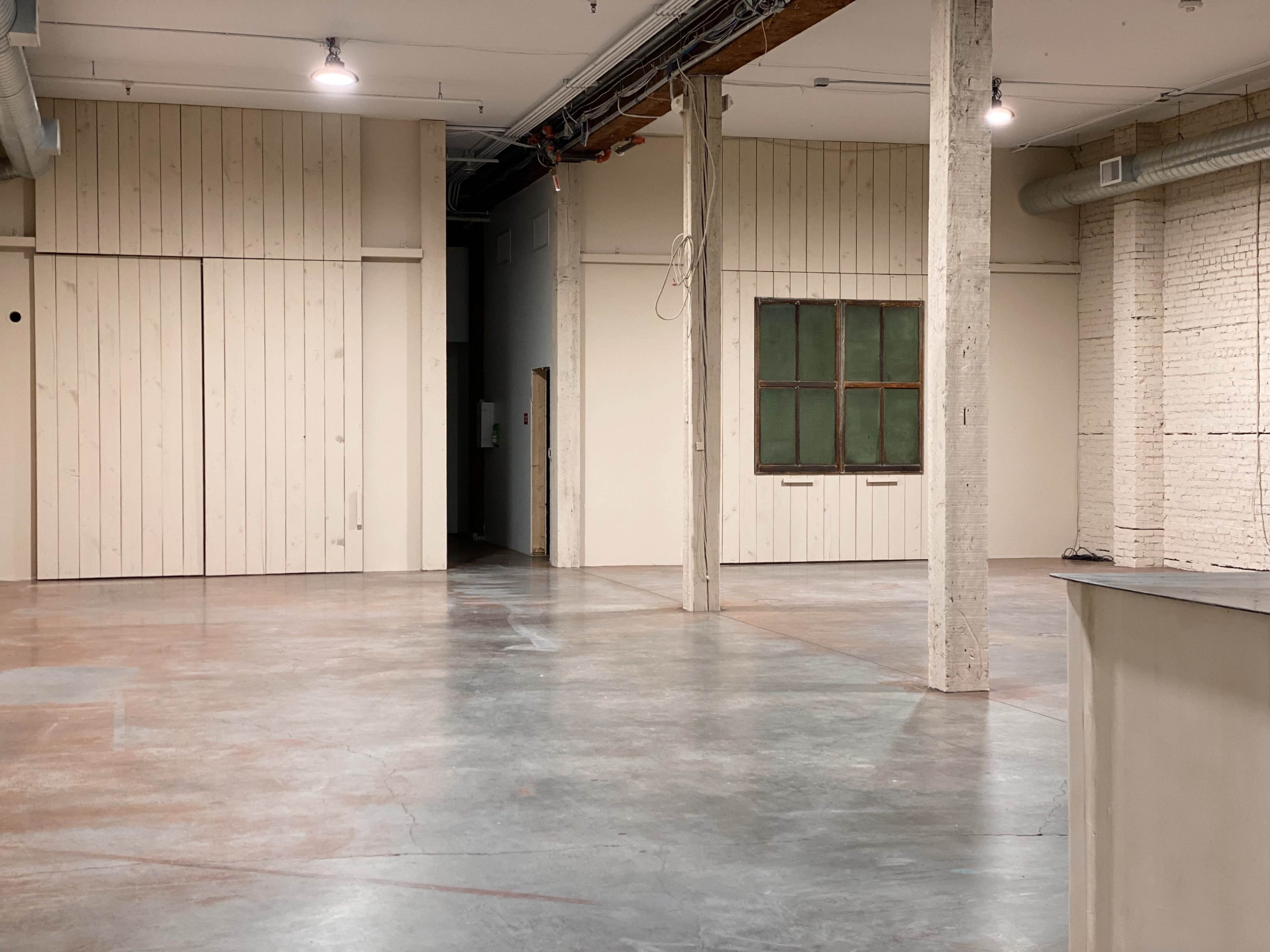 An empty industrial-style interior with a polished concrete floor, exposed brick walls, and wooden paneling.