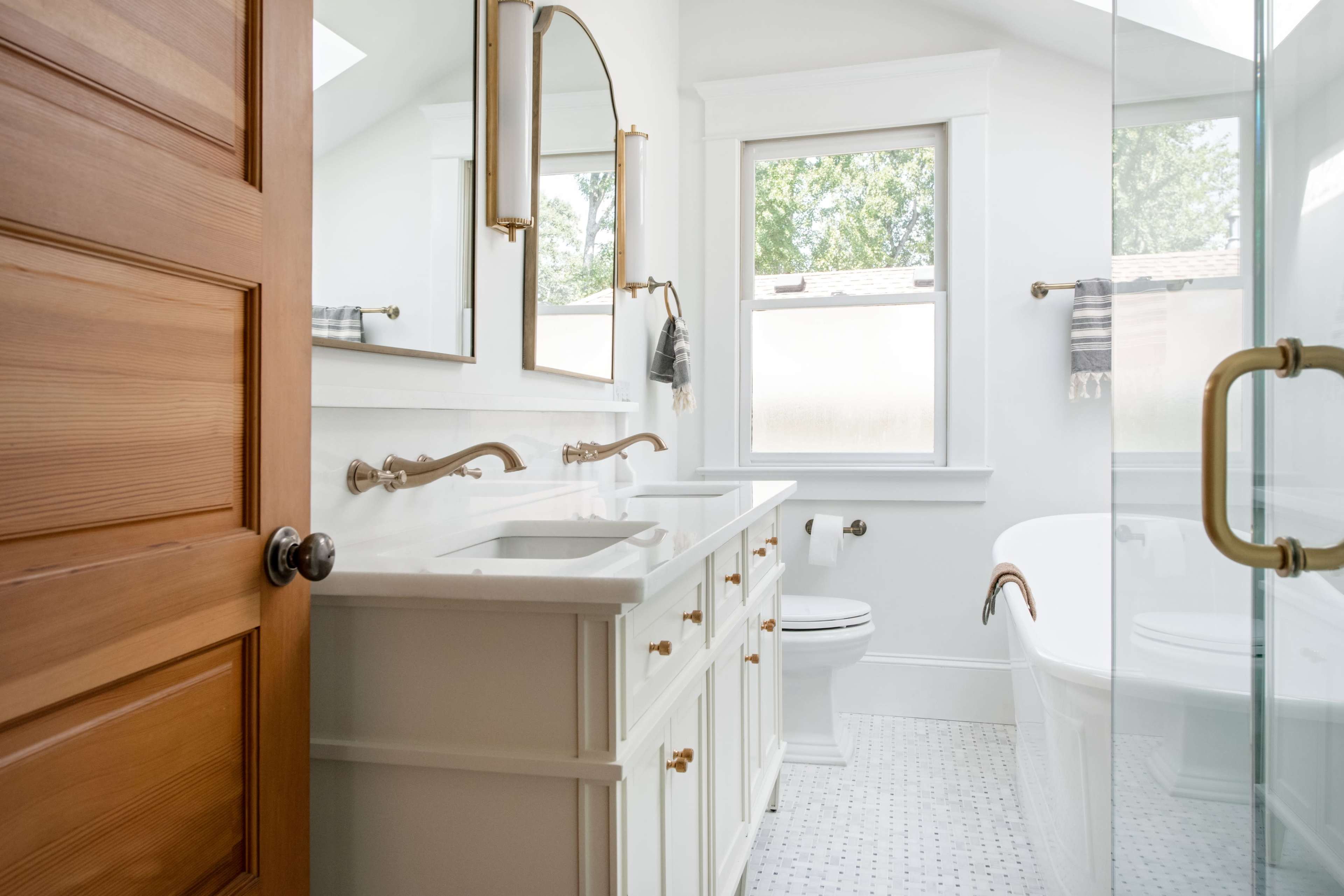 A modern bathroom features a double vanity with bronze faucets, a freestanding bathtub, and a glass shower enclosure.