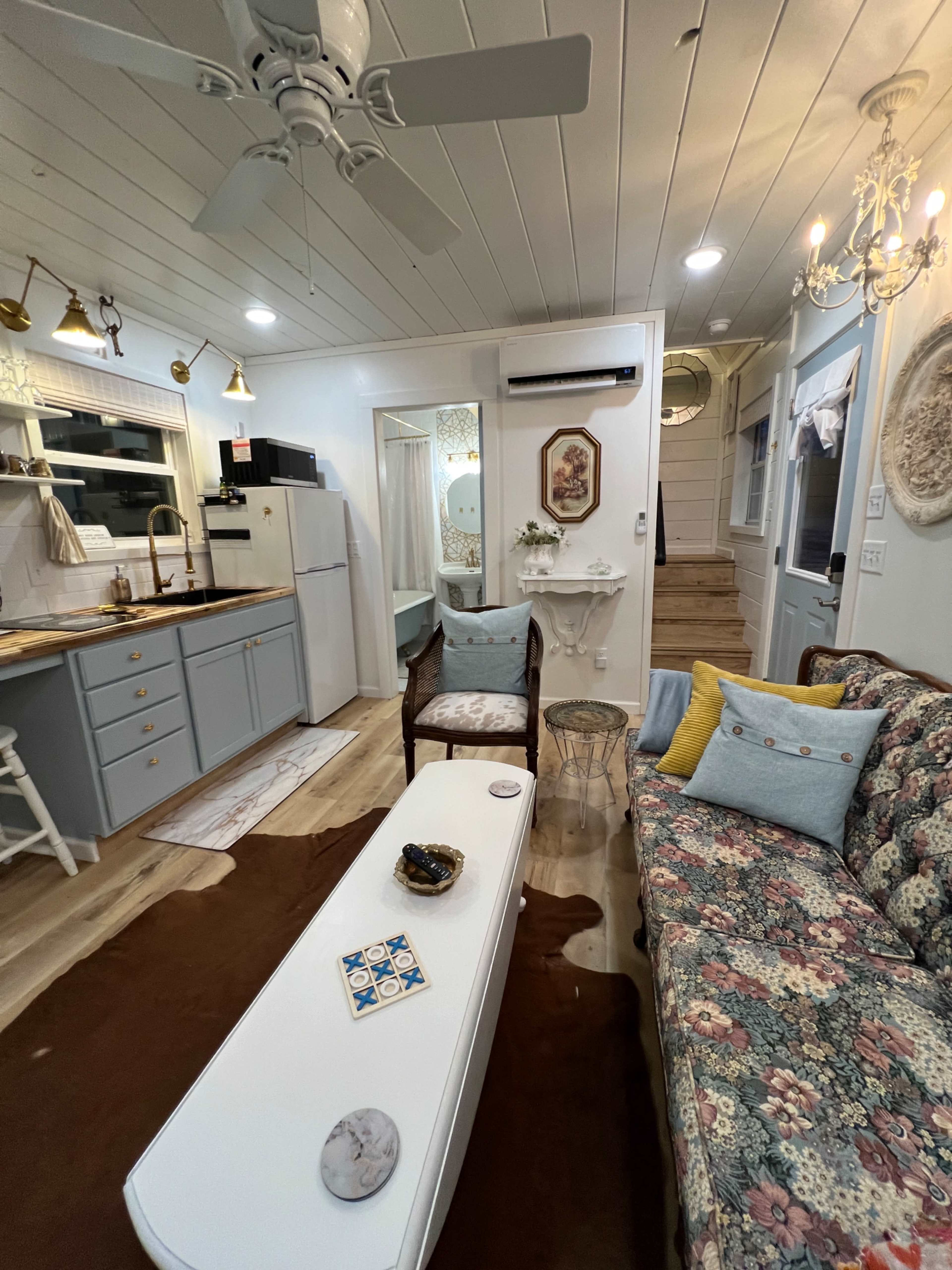 A cozy living area with a floral-patterned couch, a white coffee table, and a small dining space integrated with a kitchen in a well-lit room.