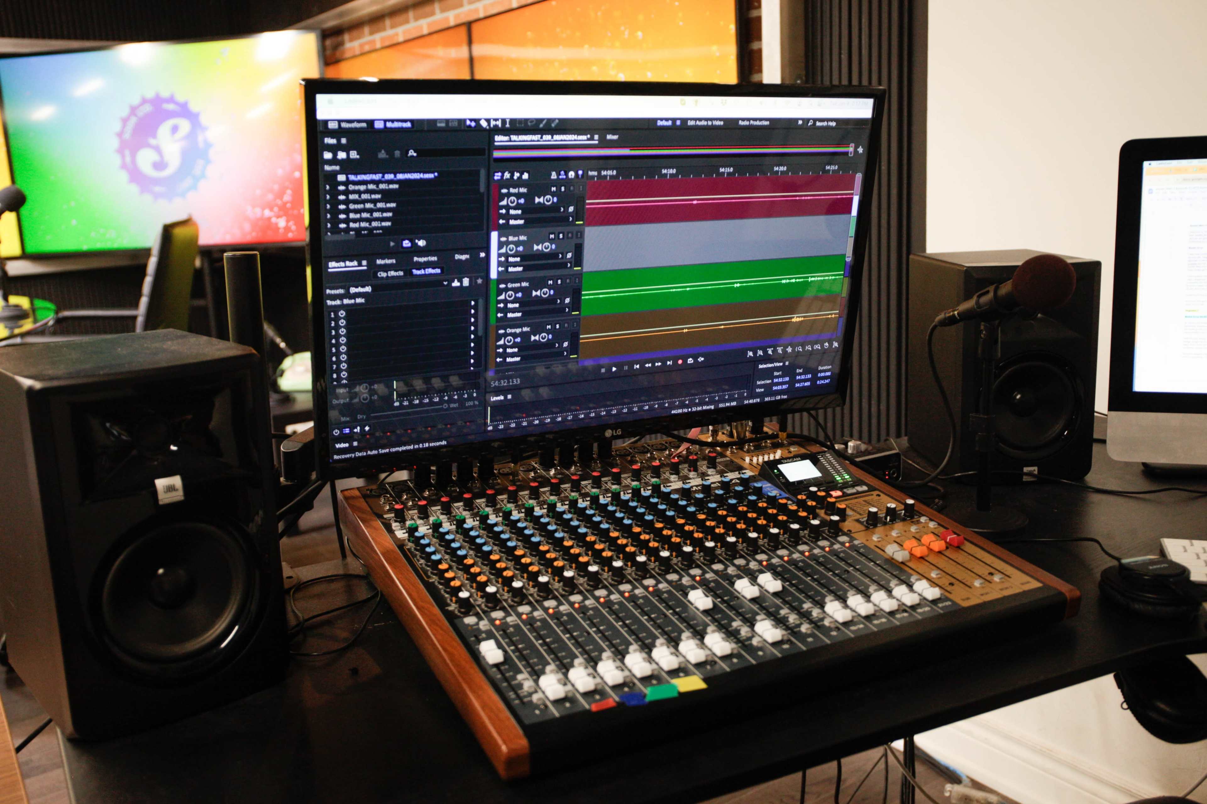 A sound mixing console with a computer screen displaying audio editing software, set in a recording studio environment.