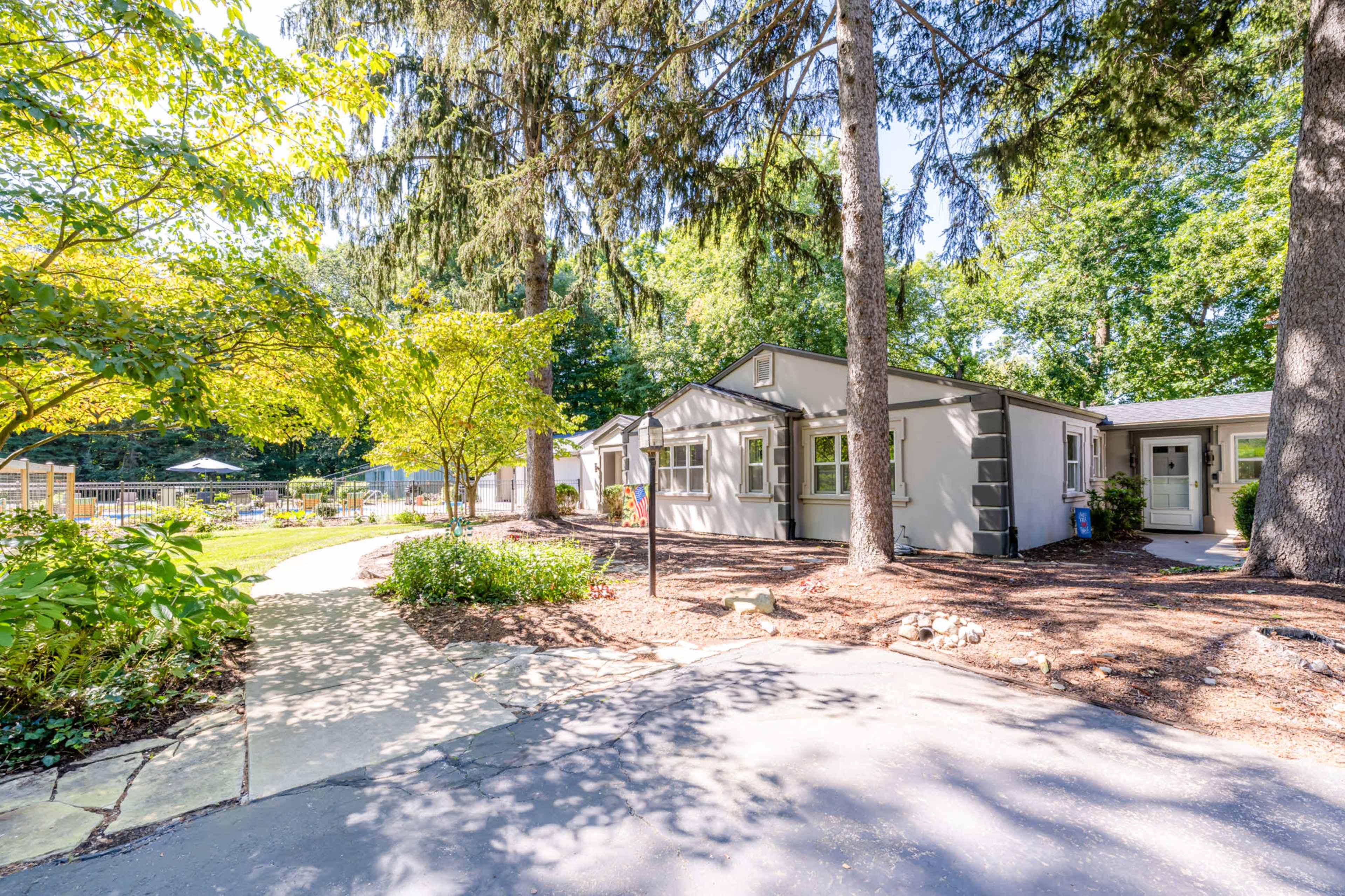A path leading to a cluster of single-story gray cottages surrounded by greenery and trees.