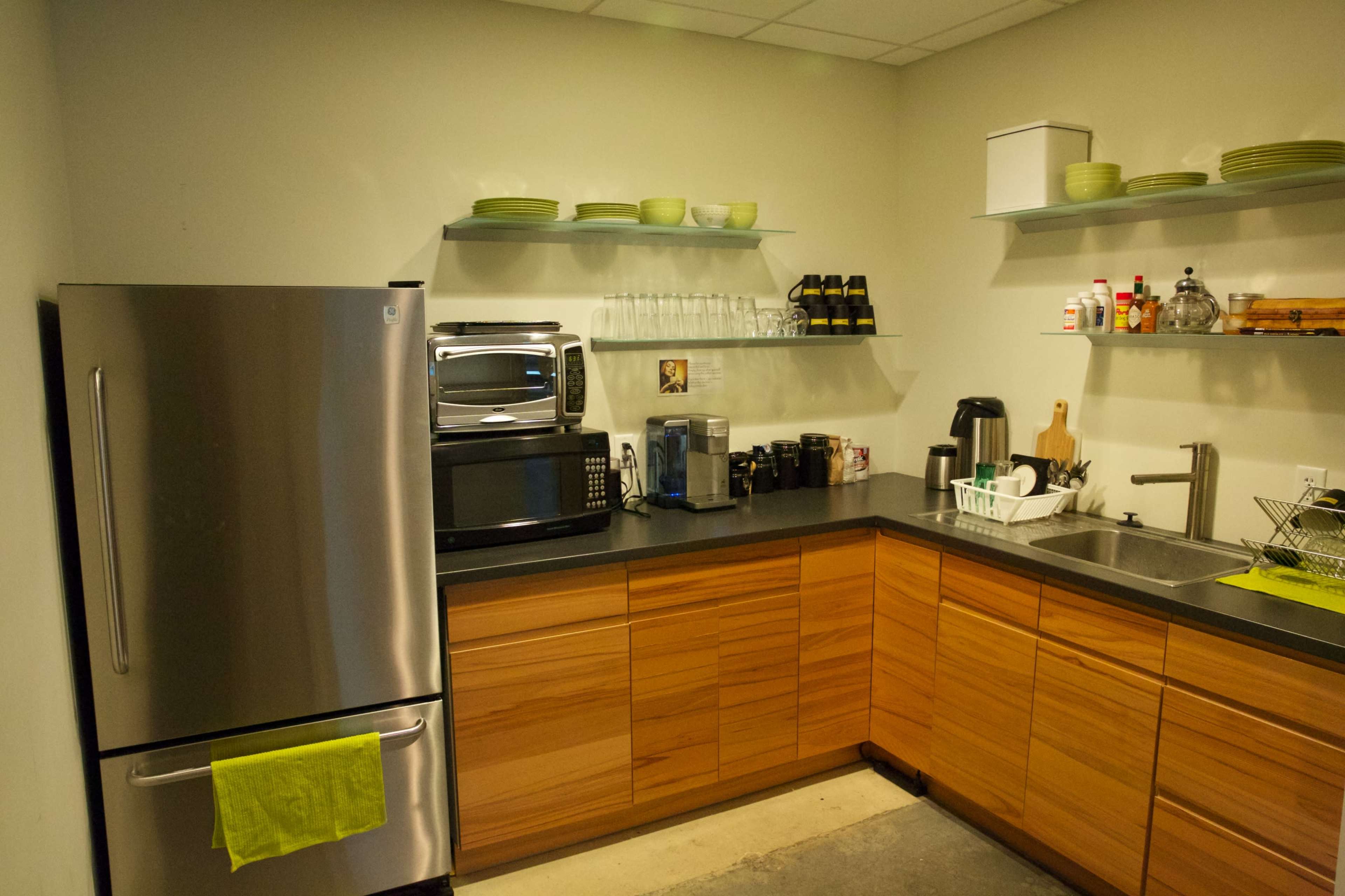 A modern kitchen with stainless steel appliances, wooden cabinets, glassware on shelves, and a sink area.