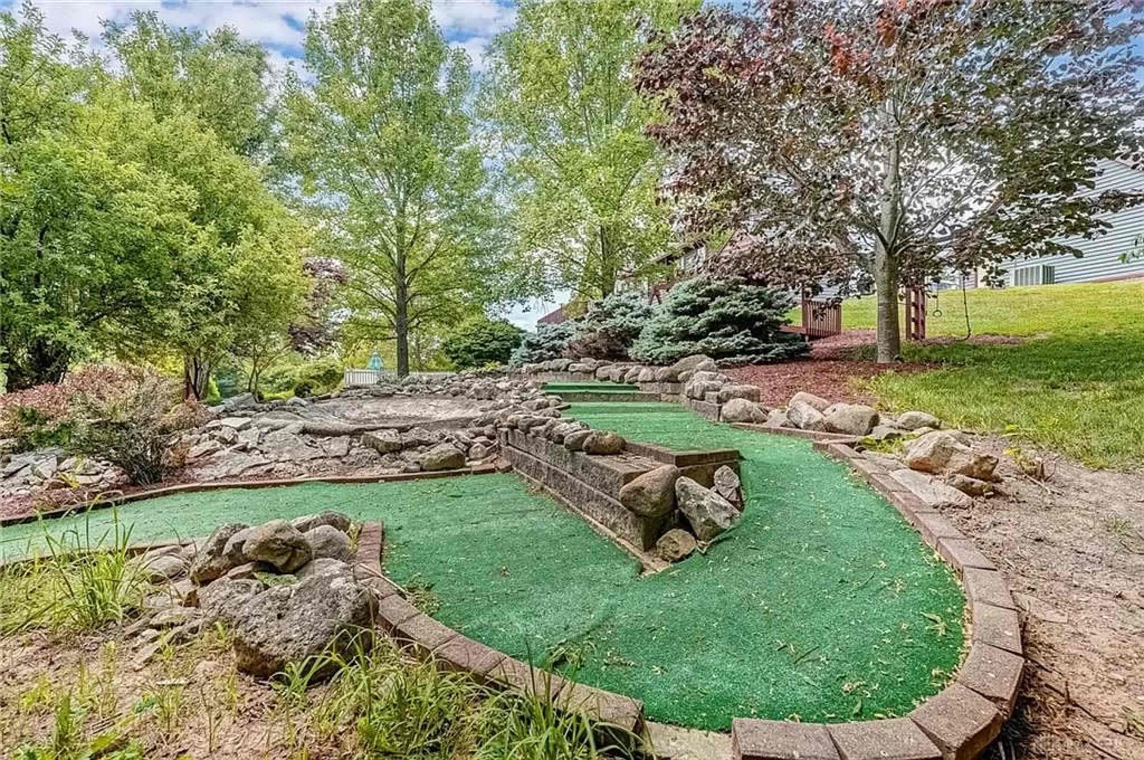 A miniature golf course featuring a winding green carpet path bordered by rocks and surrounded by trees.