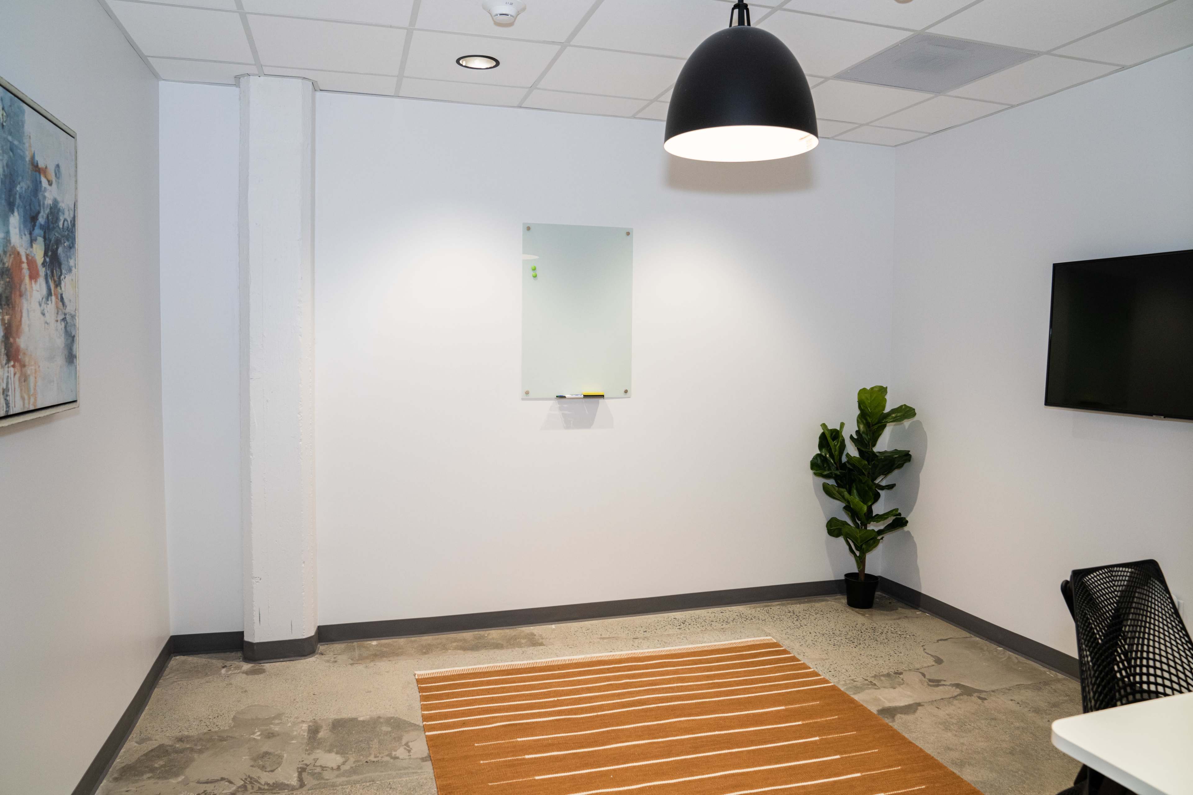 A minimalistic room with a wall-mounted whiteboard, a small plant, a light fixture, and a striped rug.