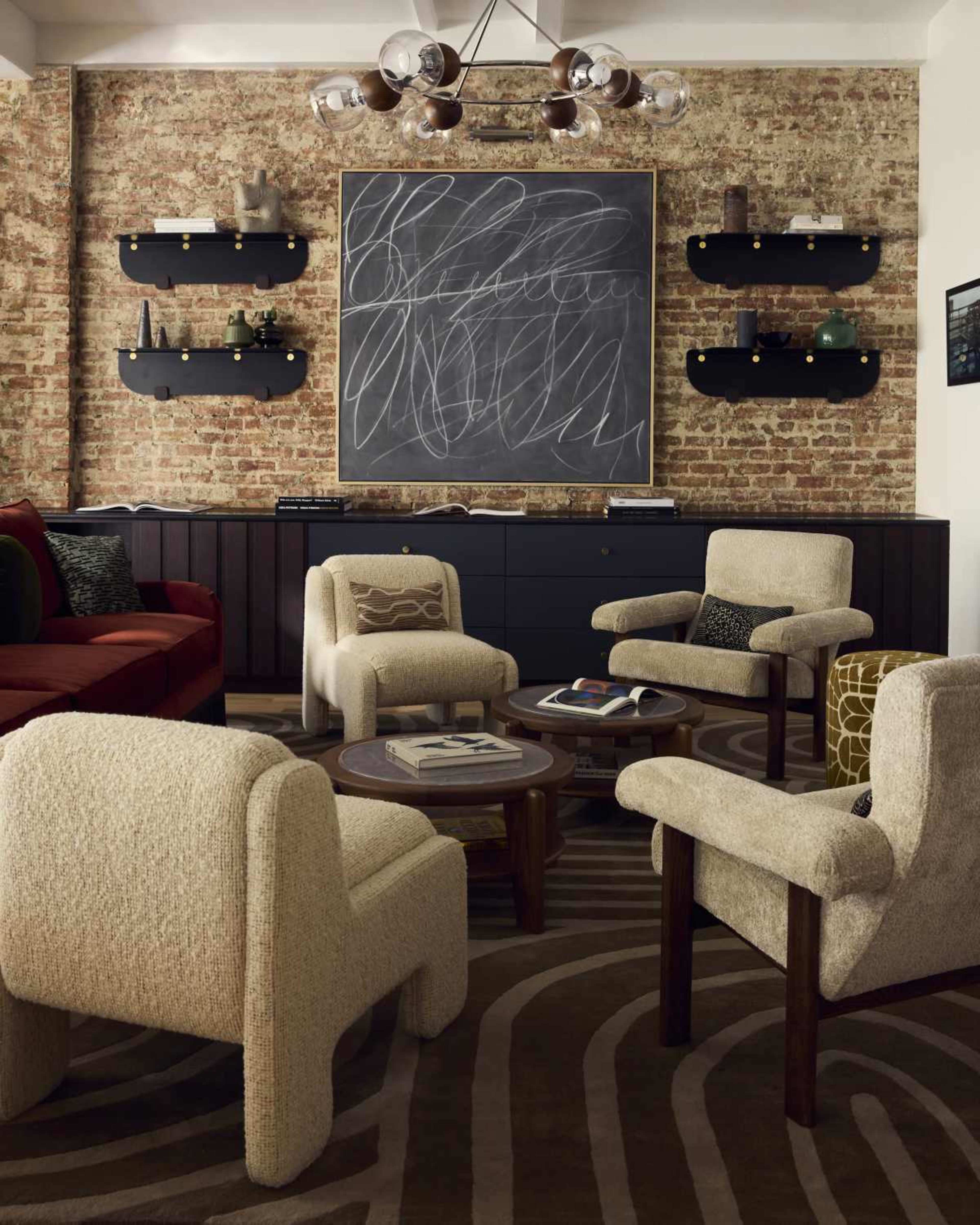A cozy living room features a brick wall, a chalkboard artwork, and four upholstered chairs arranged around a low coffee table.