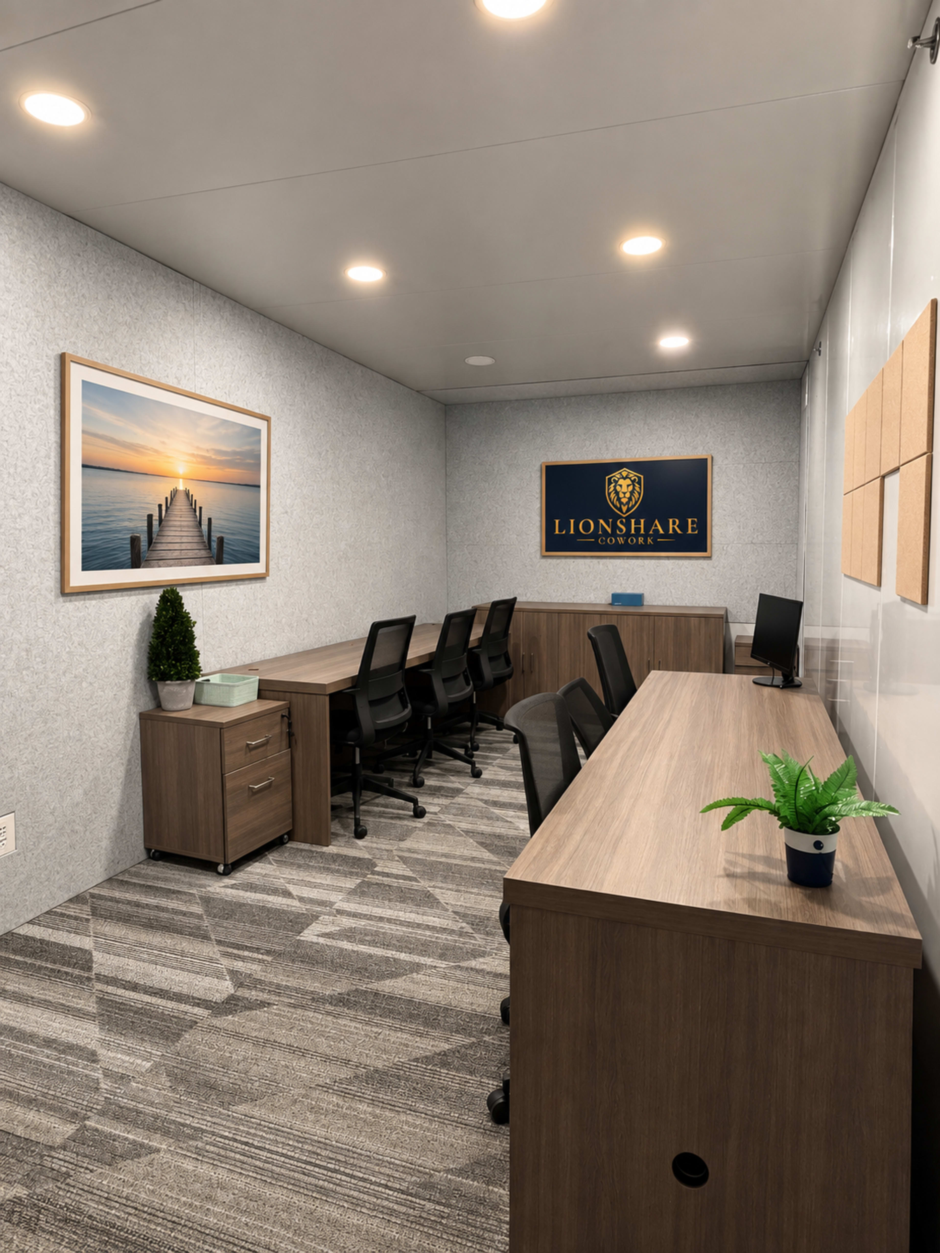 The image shows a modern office space with two long desks, four ergonomic chairs, a wall-mounted logo, a framed landscape picture, and plants for decoration.