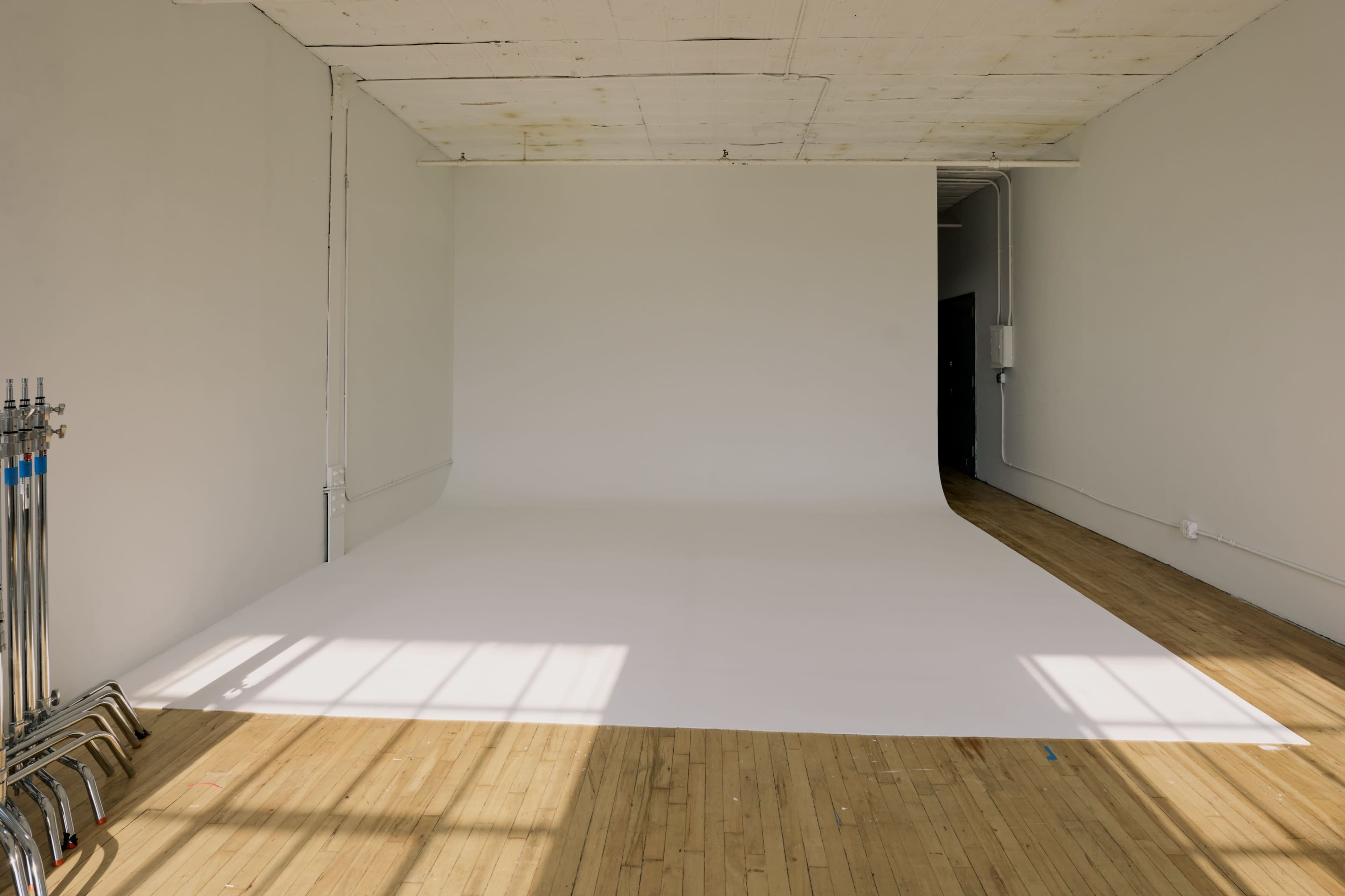 The image shows a spacious, well-lit interior with wooden flooring and a blank wall, suggesting an empty room.