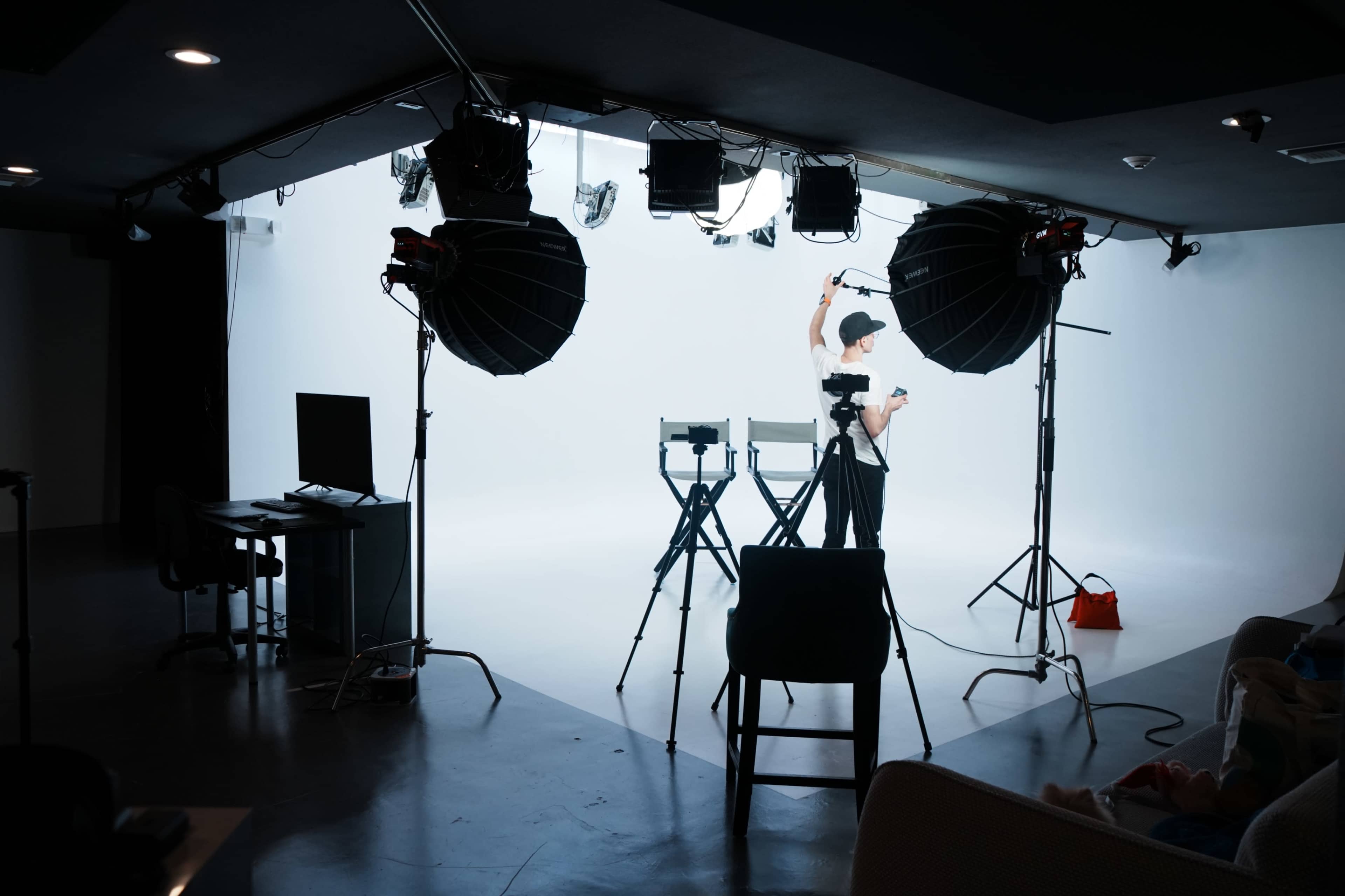 A person is preparing for a shoot in a studio equipped with lighting and two director's chairs against a blank backdrop.