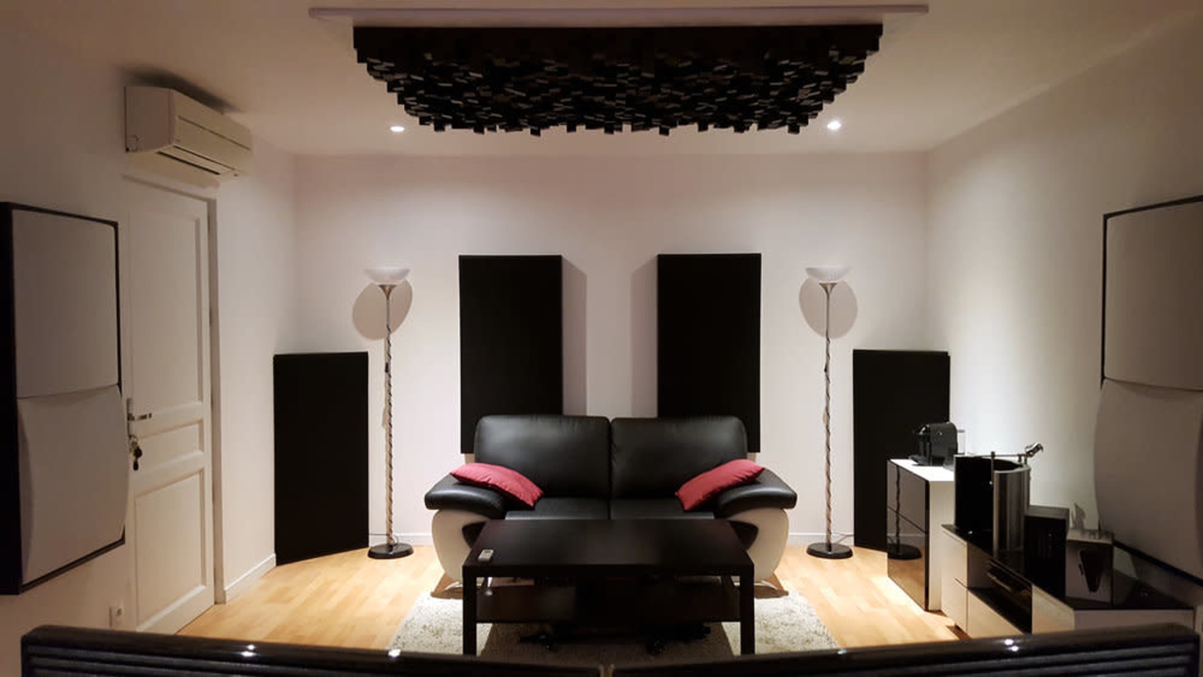 A modern living room with a black leather sofa, a coffee table, and several acoustic panels on the walls.