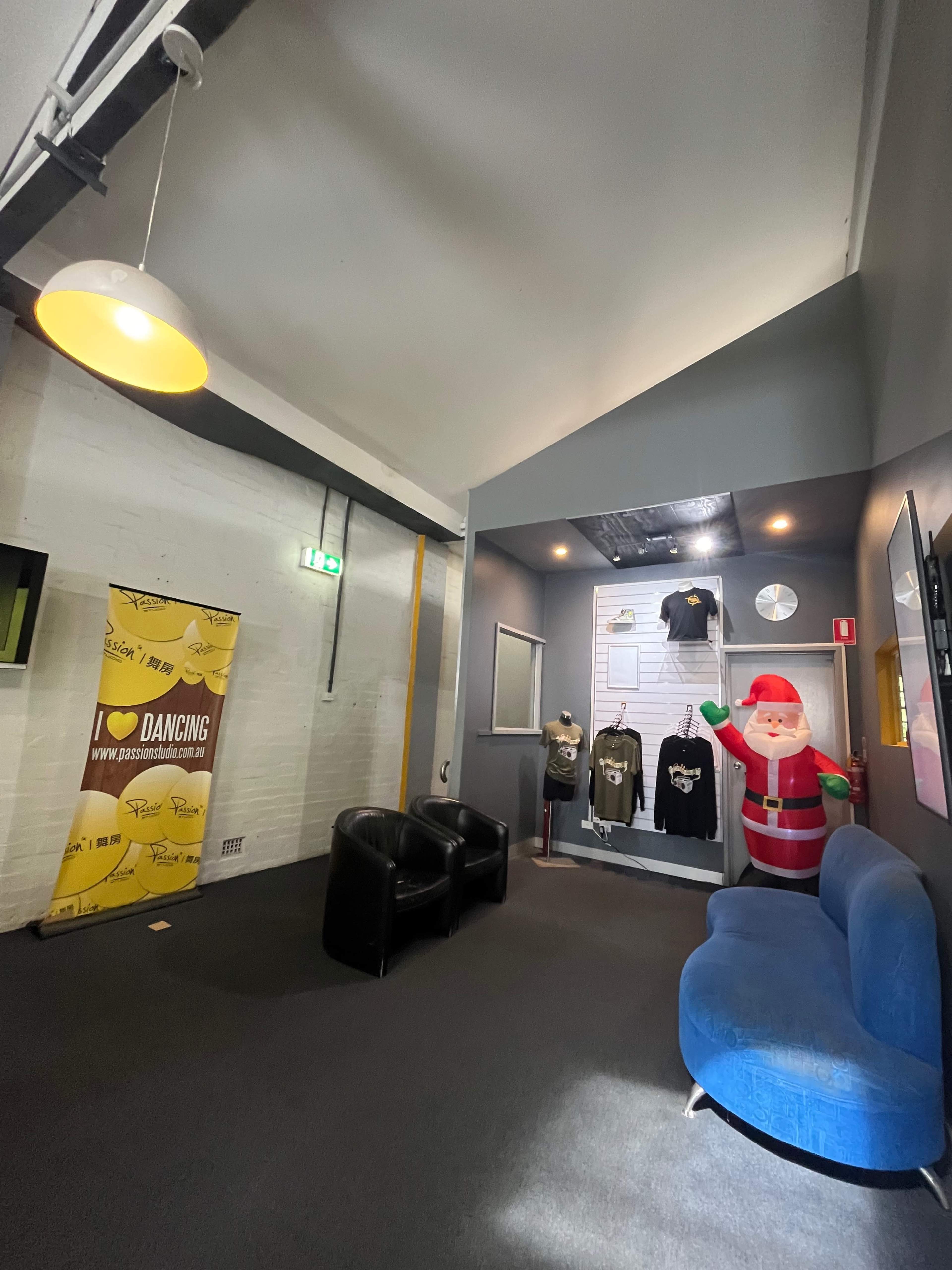 The image shows an interior space with a blue sofa, two black chairs, festive decorations, and a life-sized inflatable Santa Claus alongside a promotional banner and T-shirts on display.