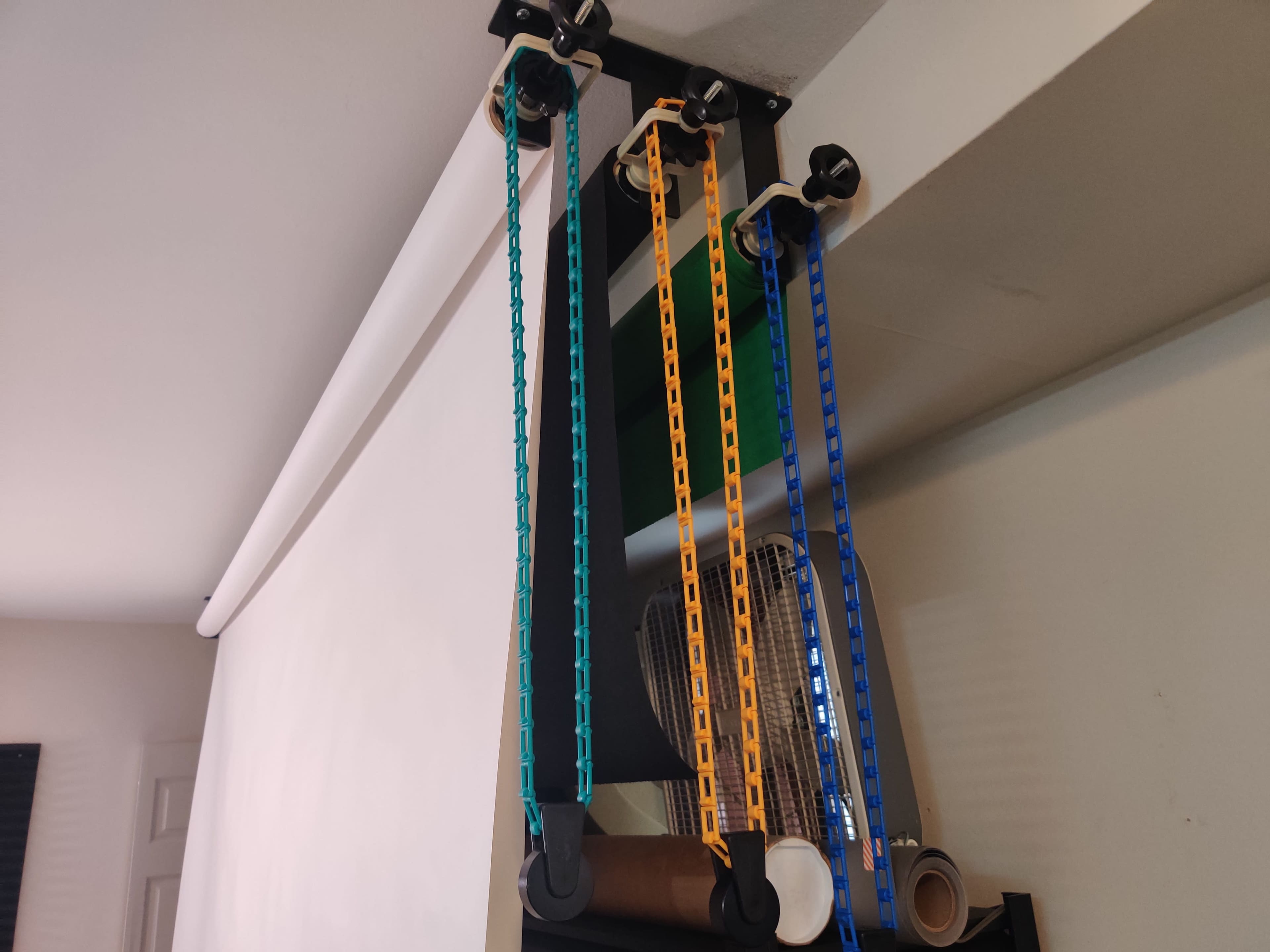 The image shows a ceiling-mounted screen with colorful chains and pulleys attached to its mechanism.