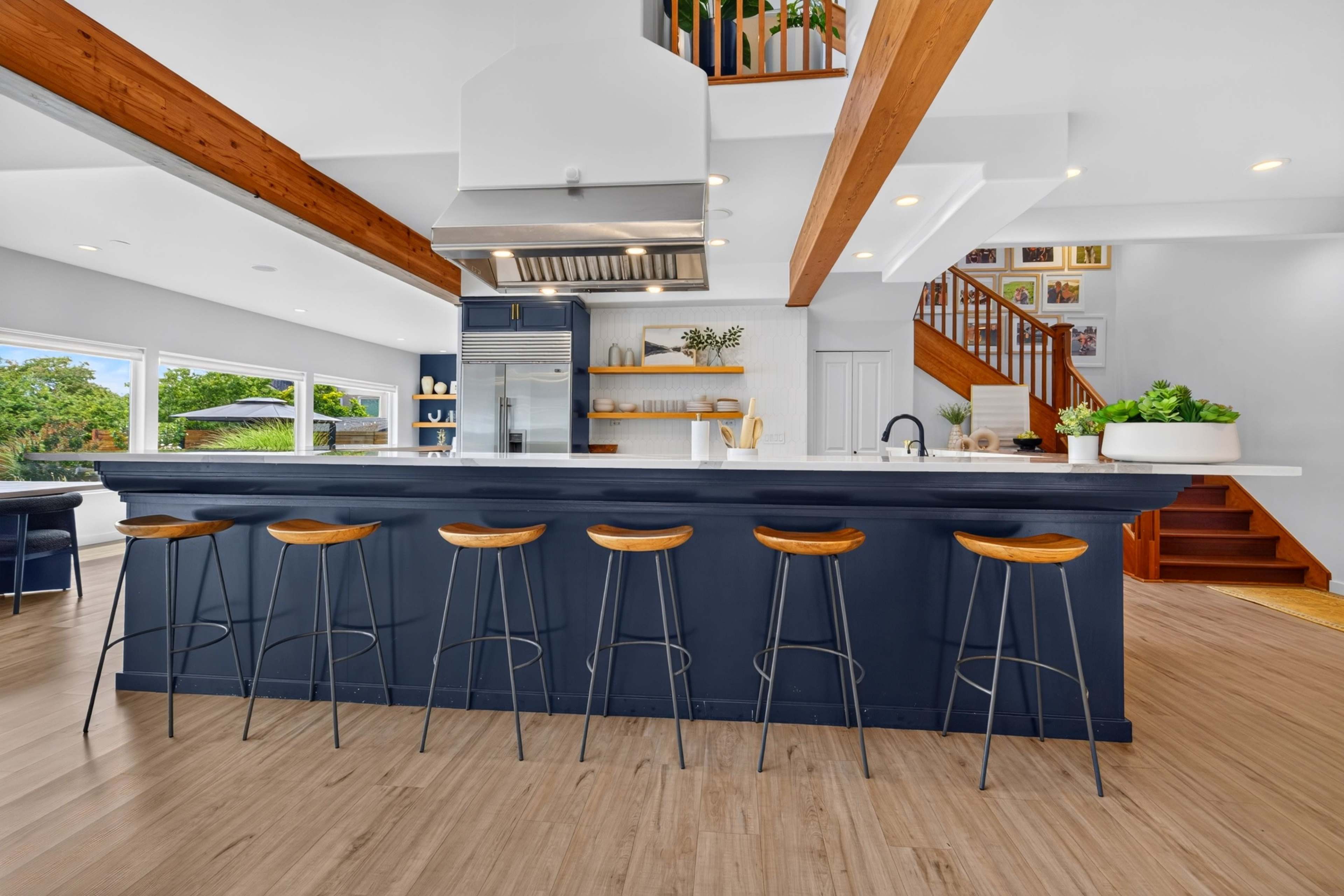A modern kitchen features a large island with bar seating, equipped with a stainless steel range hood and wooden beams overhead.