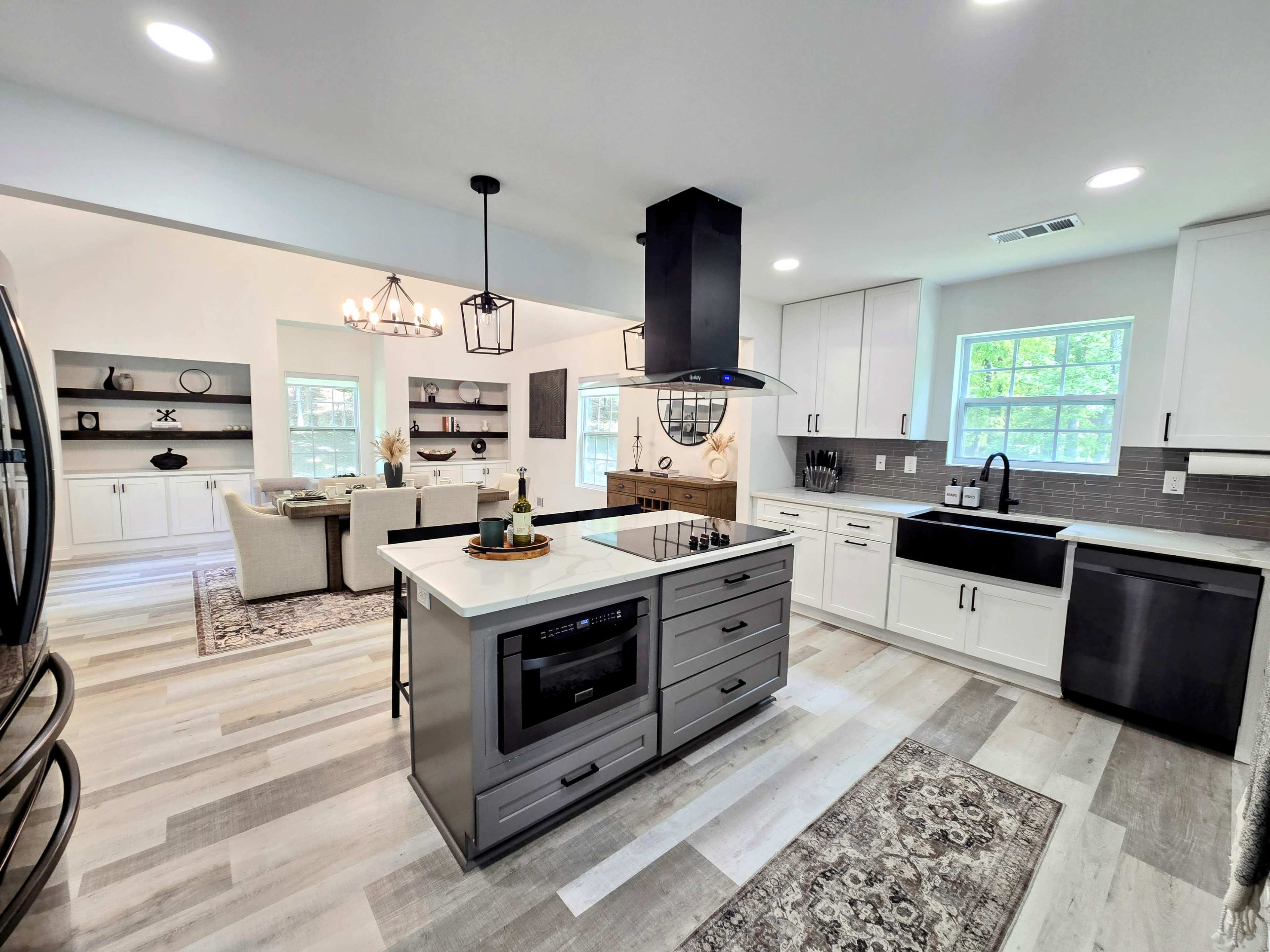 The image shows a modern kitchen with a central island, black appliances, and an open layout connecting to a living space.