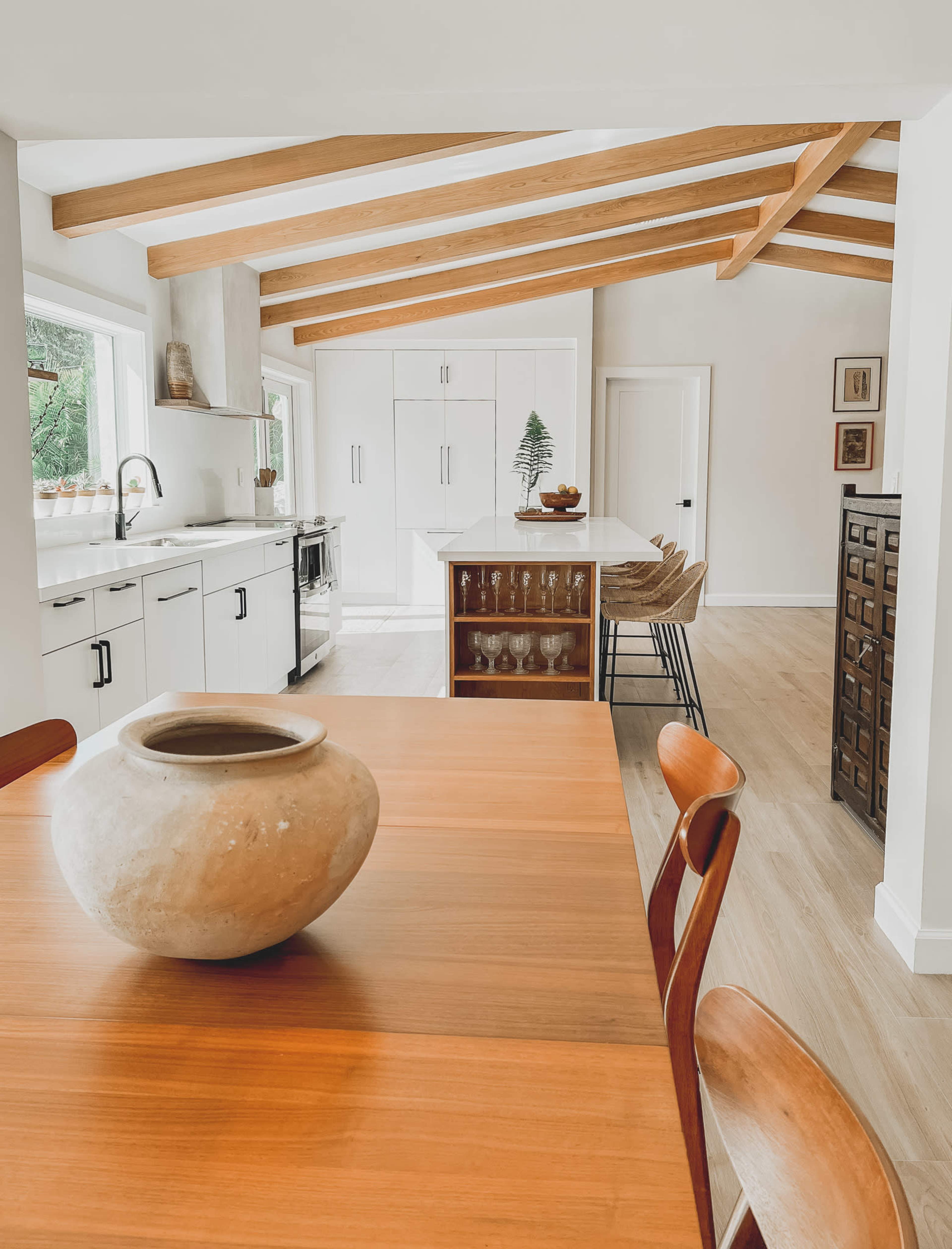 A modern kitchen with wooden beams, a dining table in the foreground, and sleek cabinetry in the background.