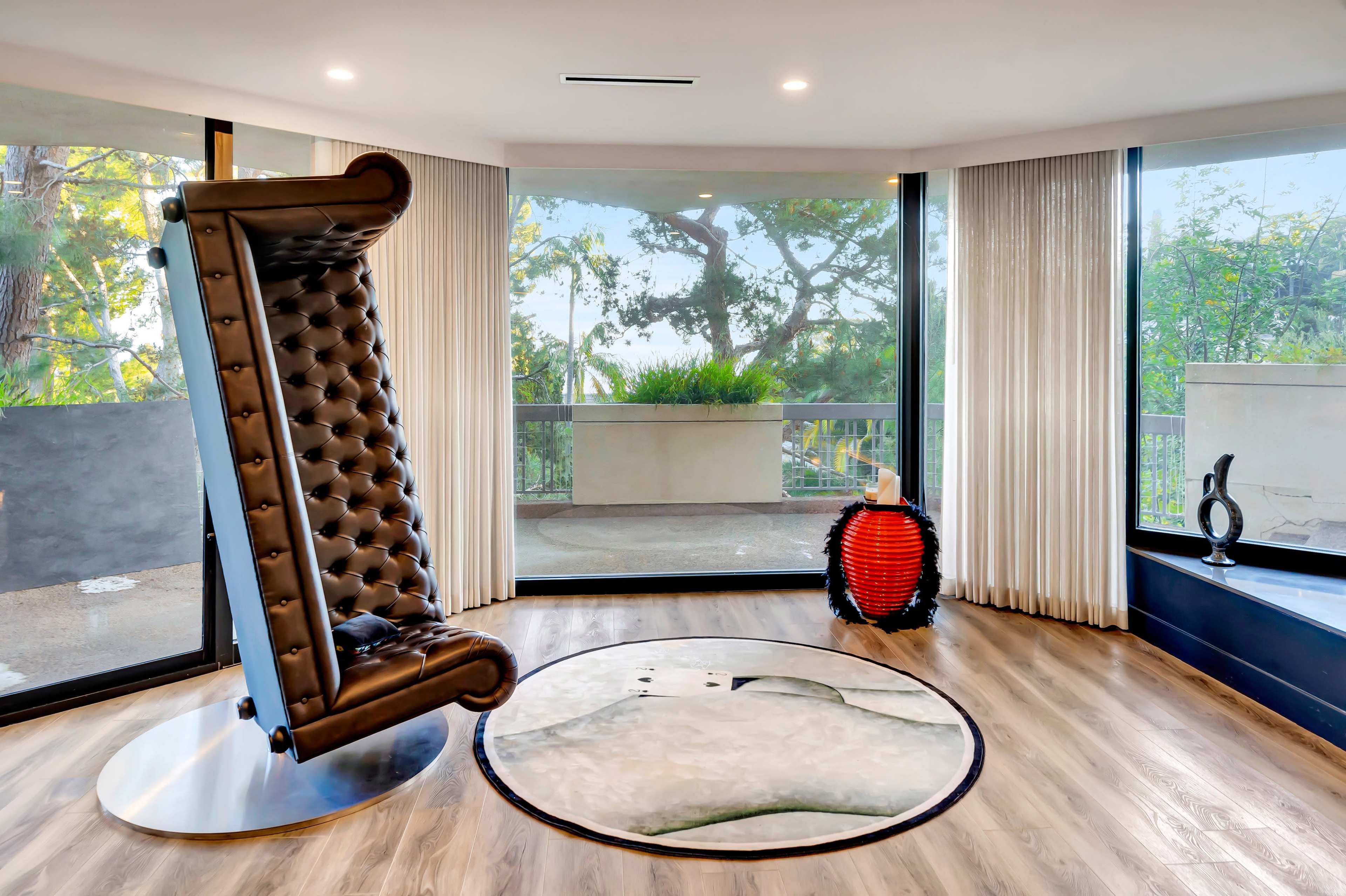 A modern room with large windows, showcasing a uniquely designed upright chair and a round rug on a hardwood floor.