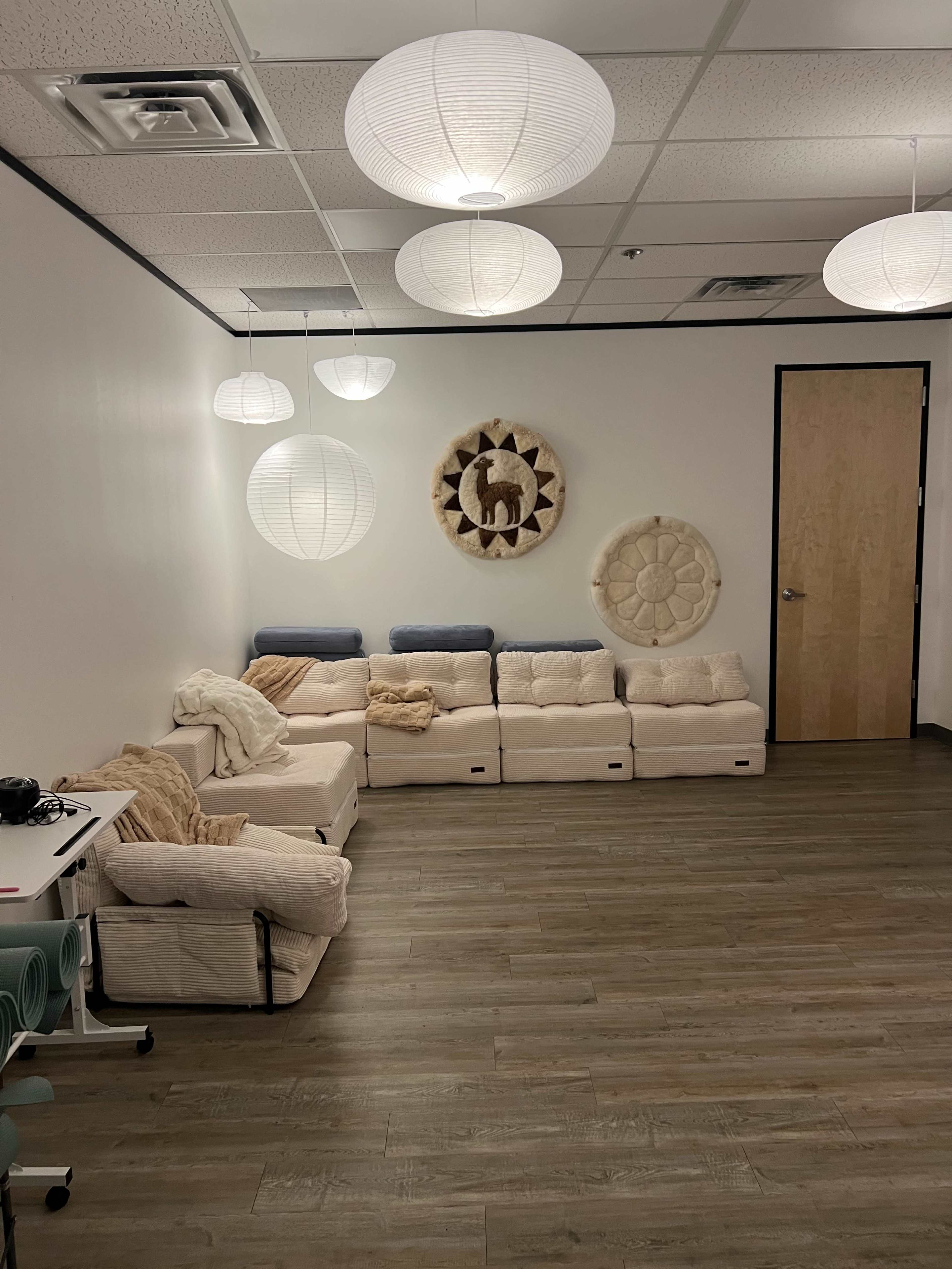 The image depicts a softly lit room featuring a modular white couch arrangement and decorative wall hangings, with pendant lights overhead.