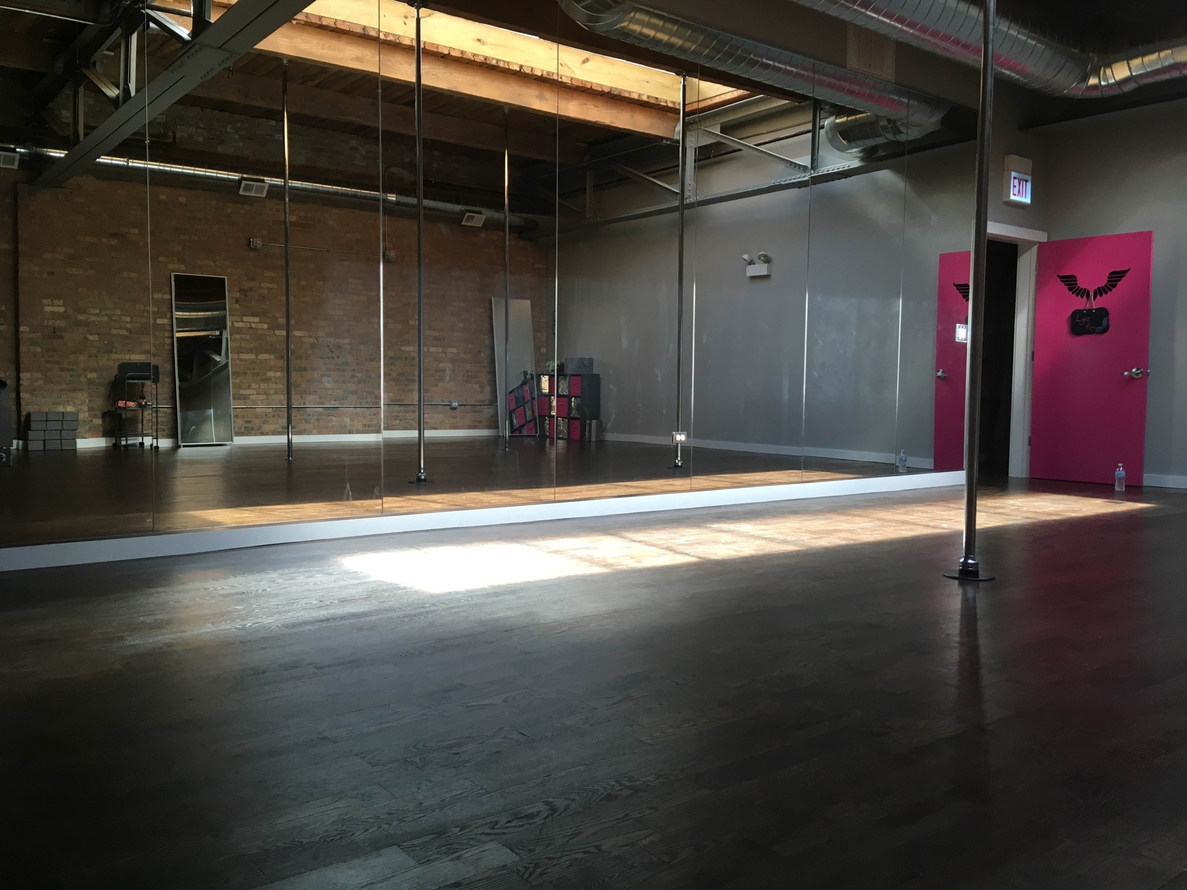 A spacious dance studio with wooden floors, mirrored walls, and a bright pink door at the far end.