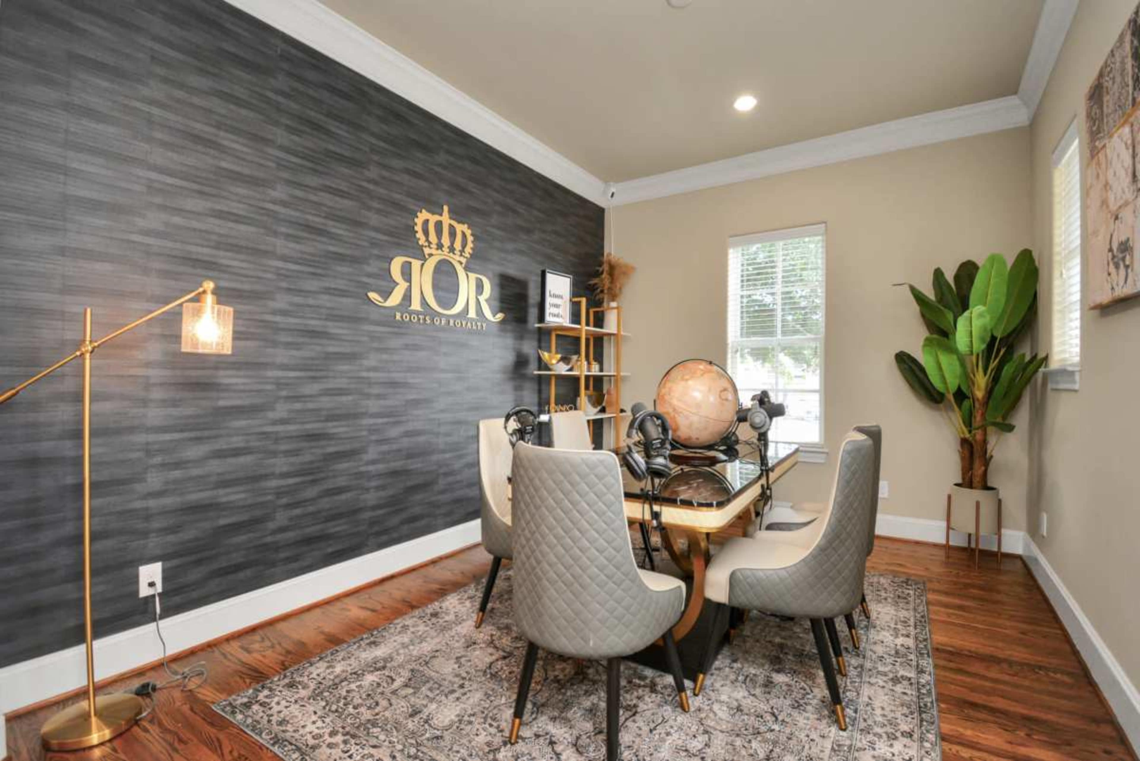The image shows a modern conference room with a large table surrounded by six chairs, a globe, a tall plant in one corner, and a decorative wall featuring a logo and artwork.