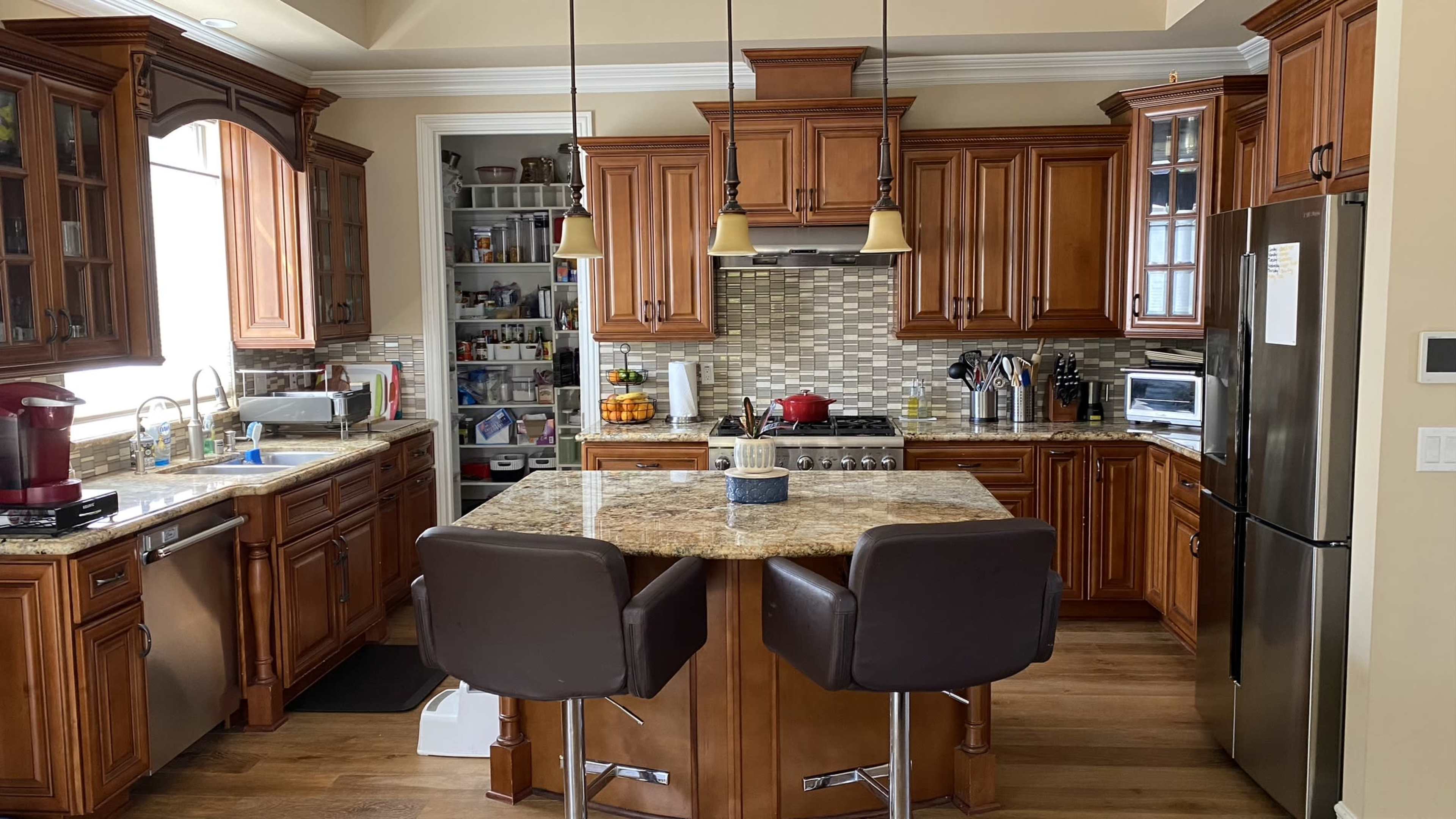 A kitchen with wooden cabinetry, granite countertops, and a central island with two chairs.