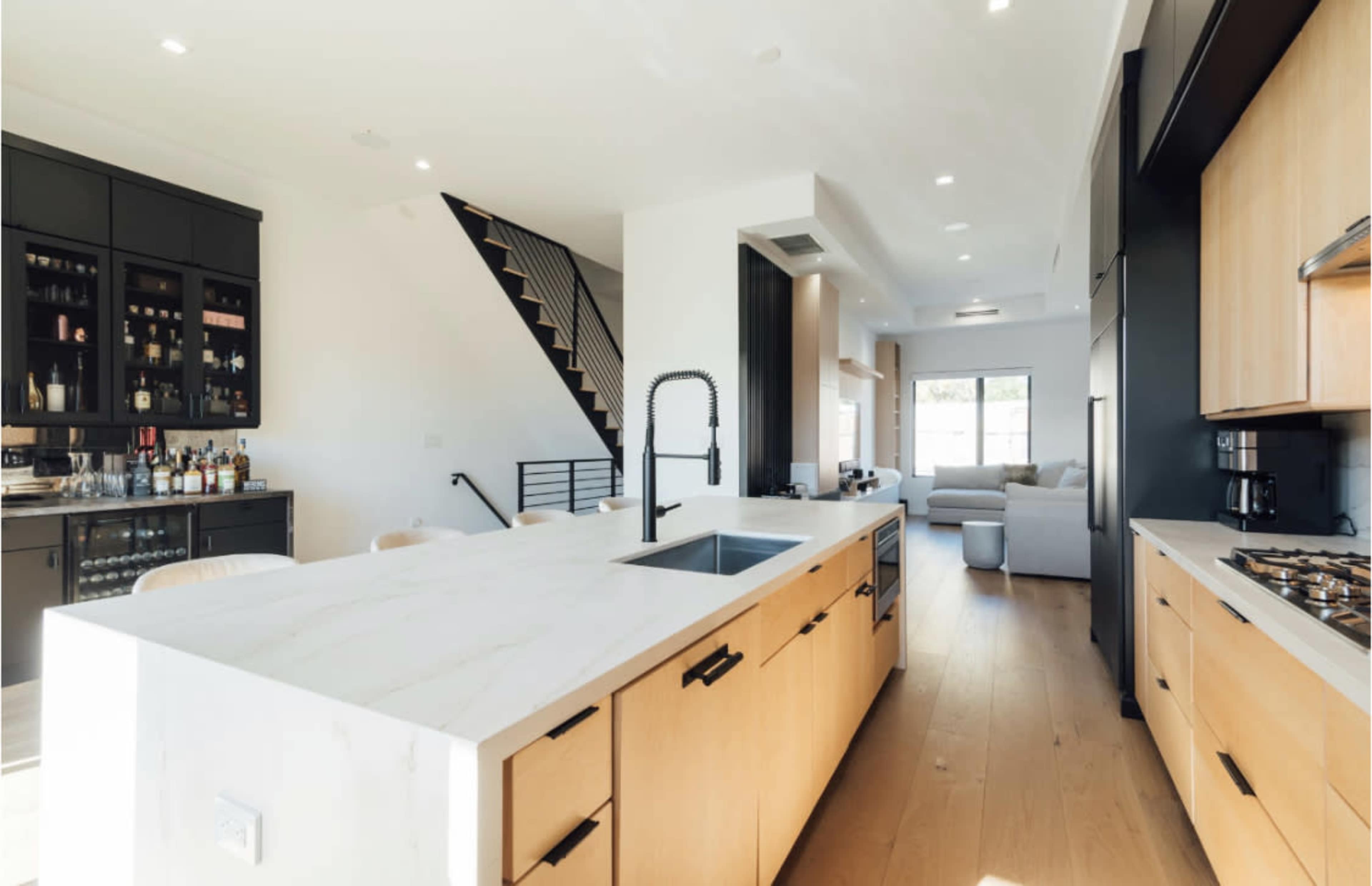 A modern kitchen with light wood cabinetry, a large marble island, and an open layout leading to a living area.