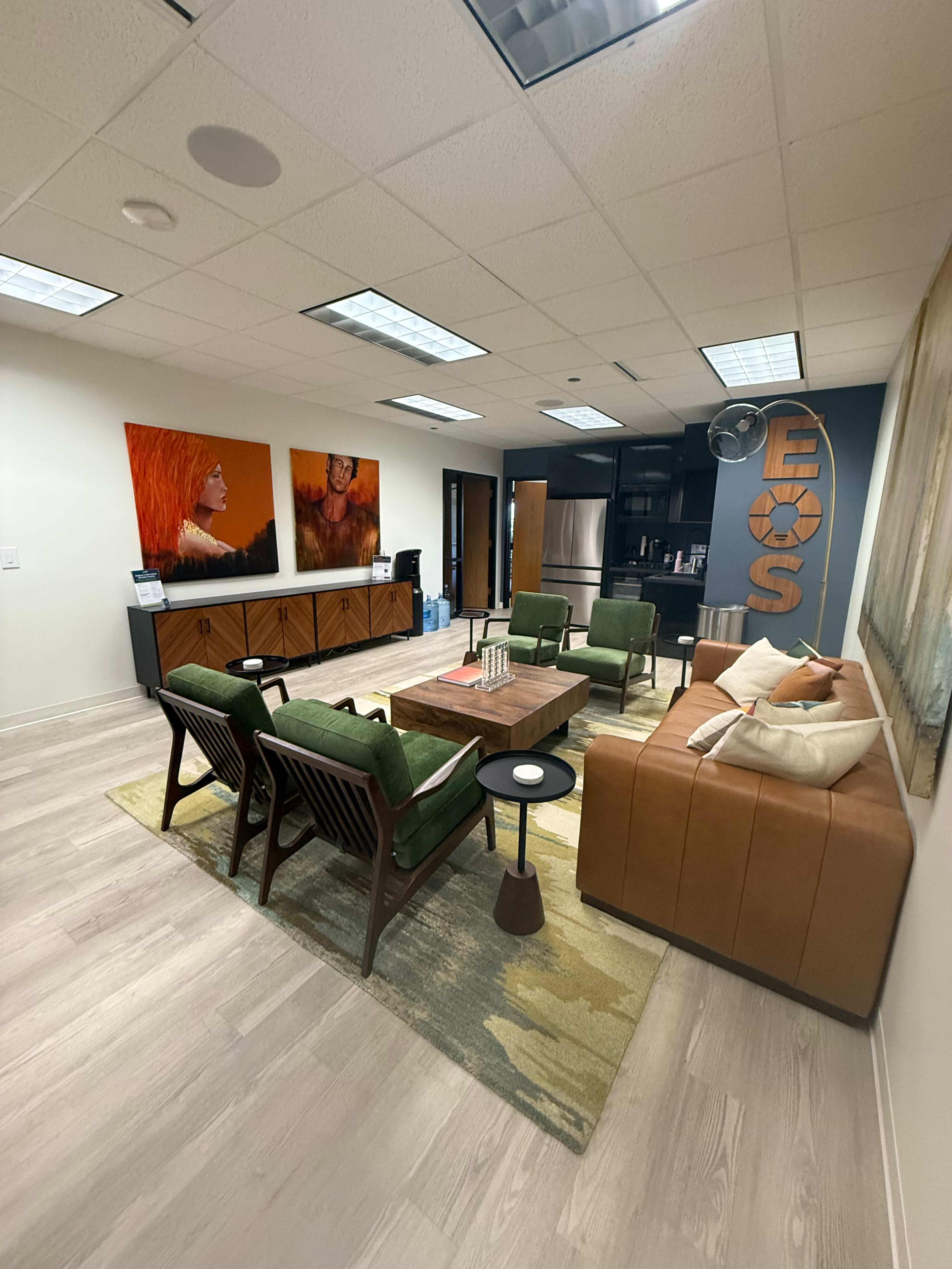 The image shows a modern office lounge area featuring a mix of seating options, a coffee table, and two large artworks on the walls.