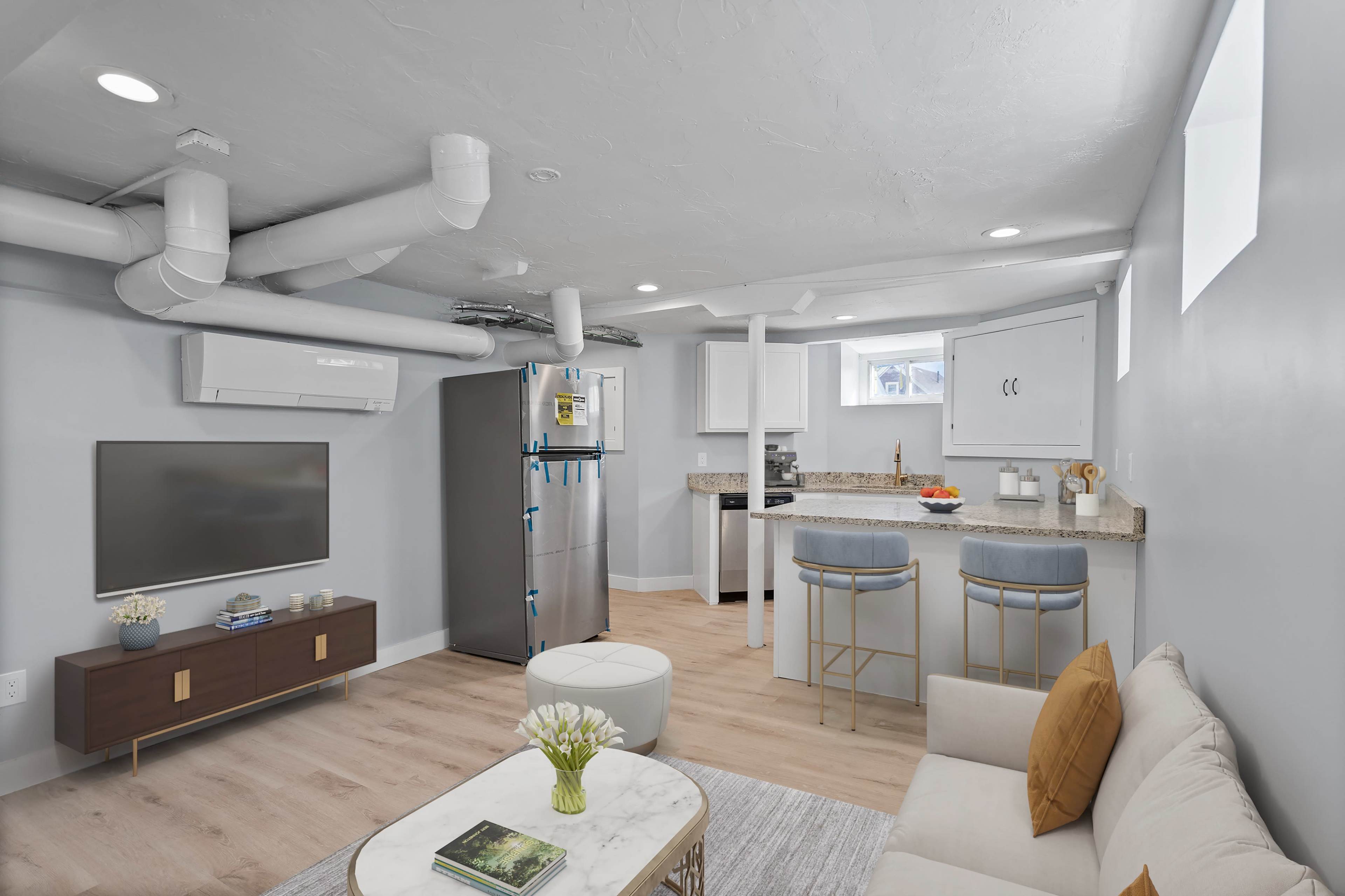 A modern, compact living space featuring a kitchen area with a refrigerator, a seating area with a sofa, and a television mounted on the wall.