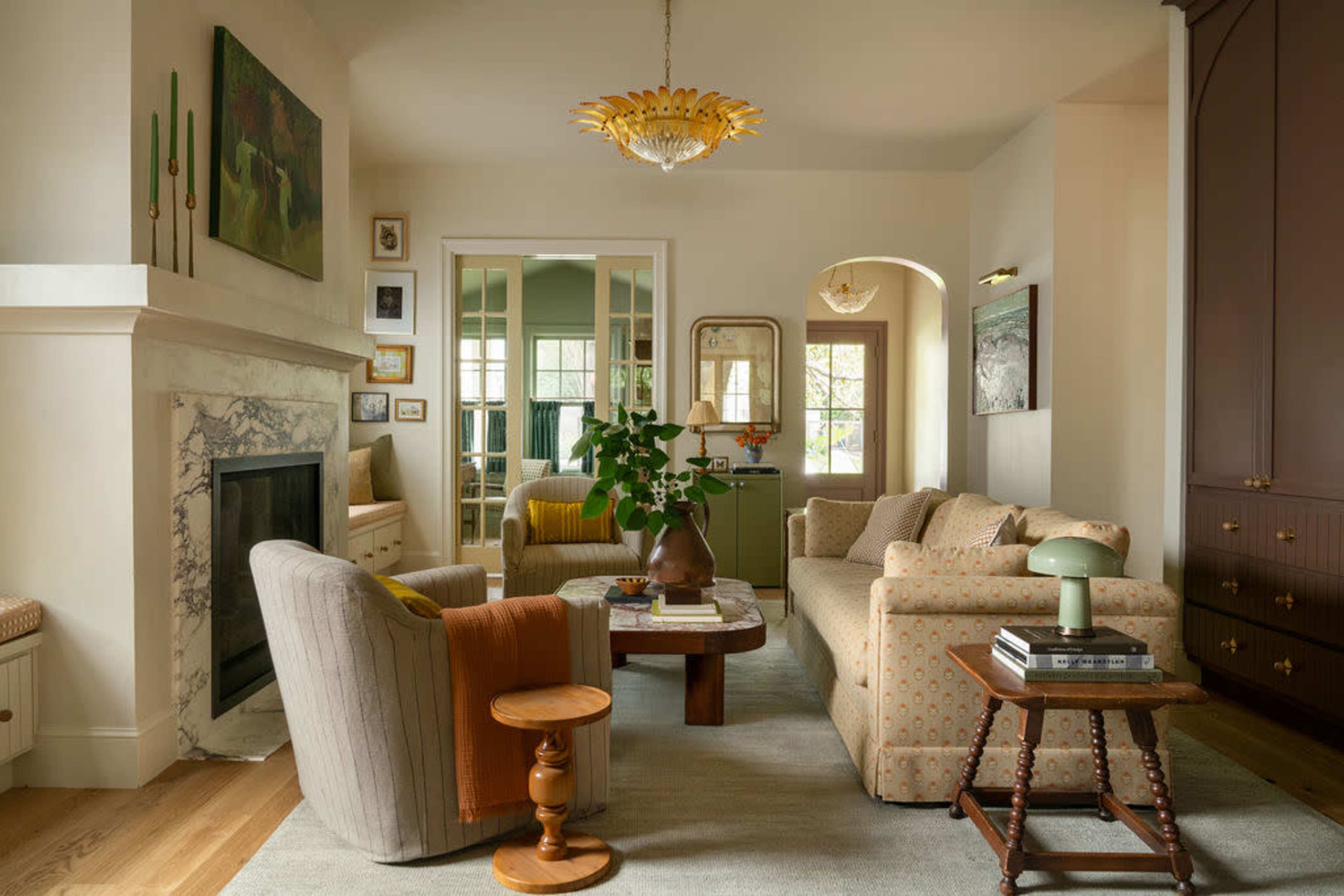 The image shows a modern living room with a patterned sofa, a stone fireplace, a coffee table, and a decorative ceiling light, surrounded by neutral-colored walls and furniture.