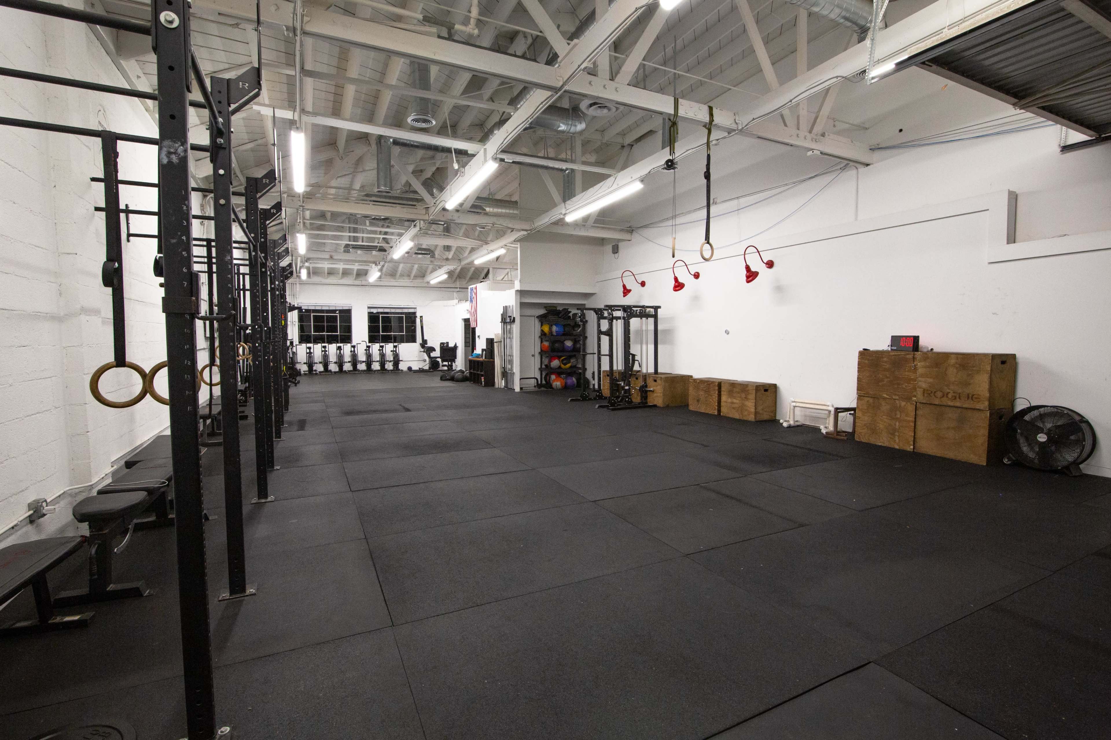 The image shows a spacious gym area equipped with weightlifting platforms, exercise rings, and various fitness equipment arranged in an organized manner.