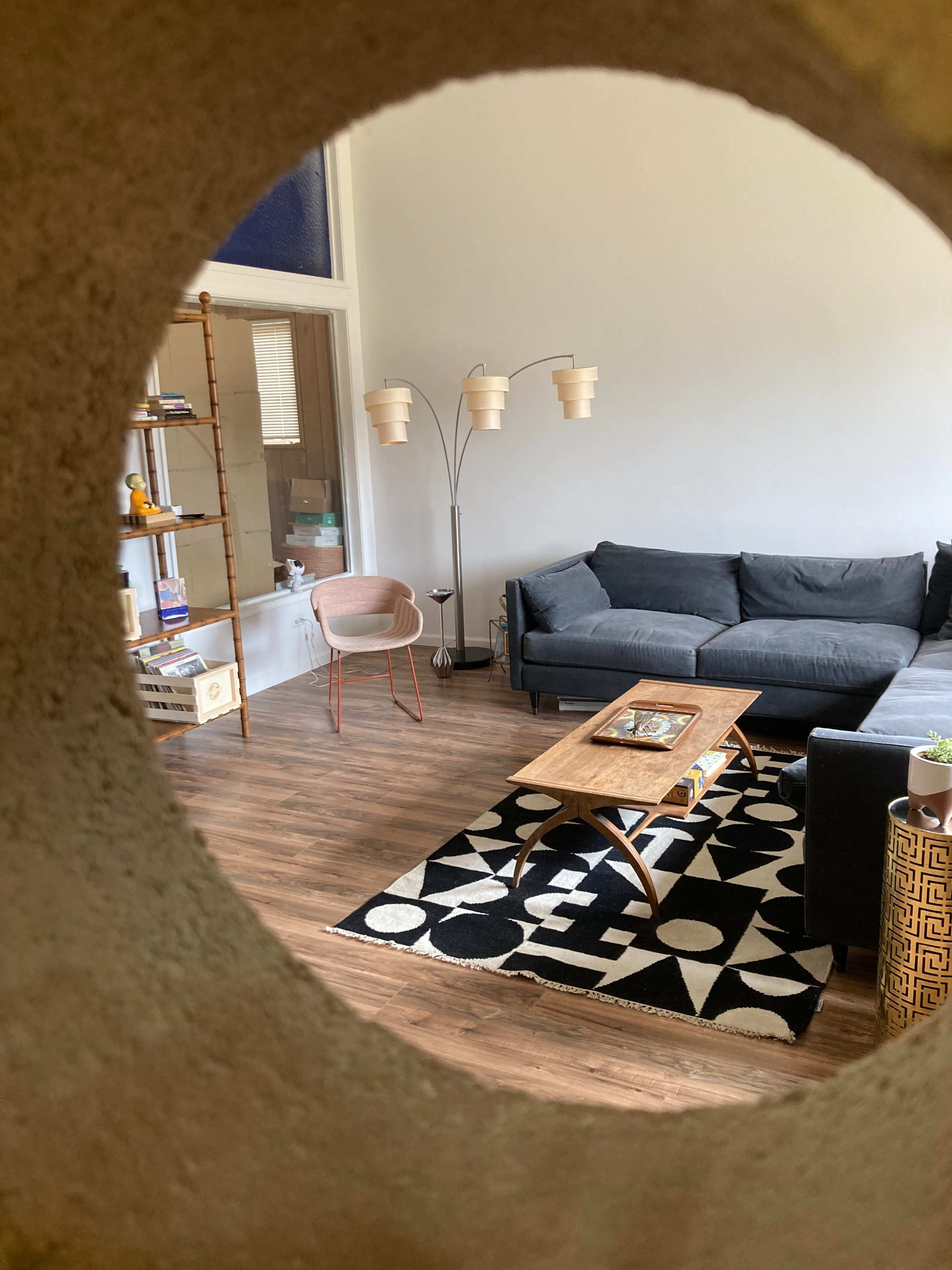 A circular opening frames a living room featuring a gray couch, a wooden coffee table on a patterned rug, and modern lighting fixtures.
