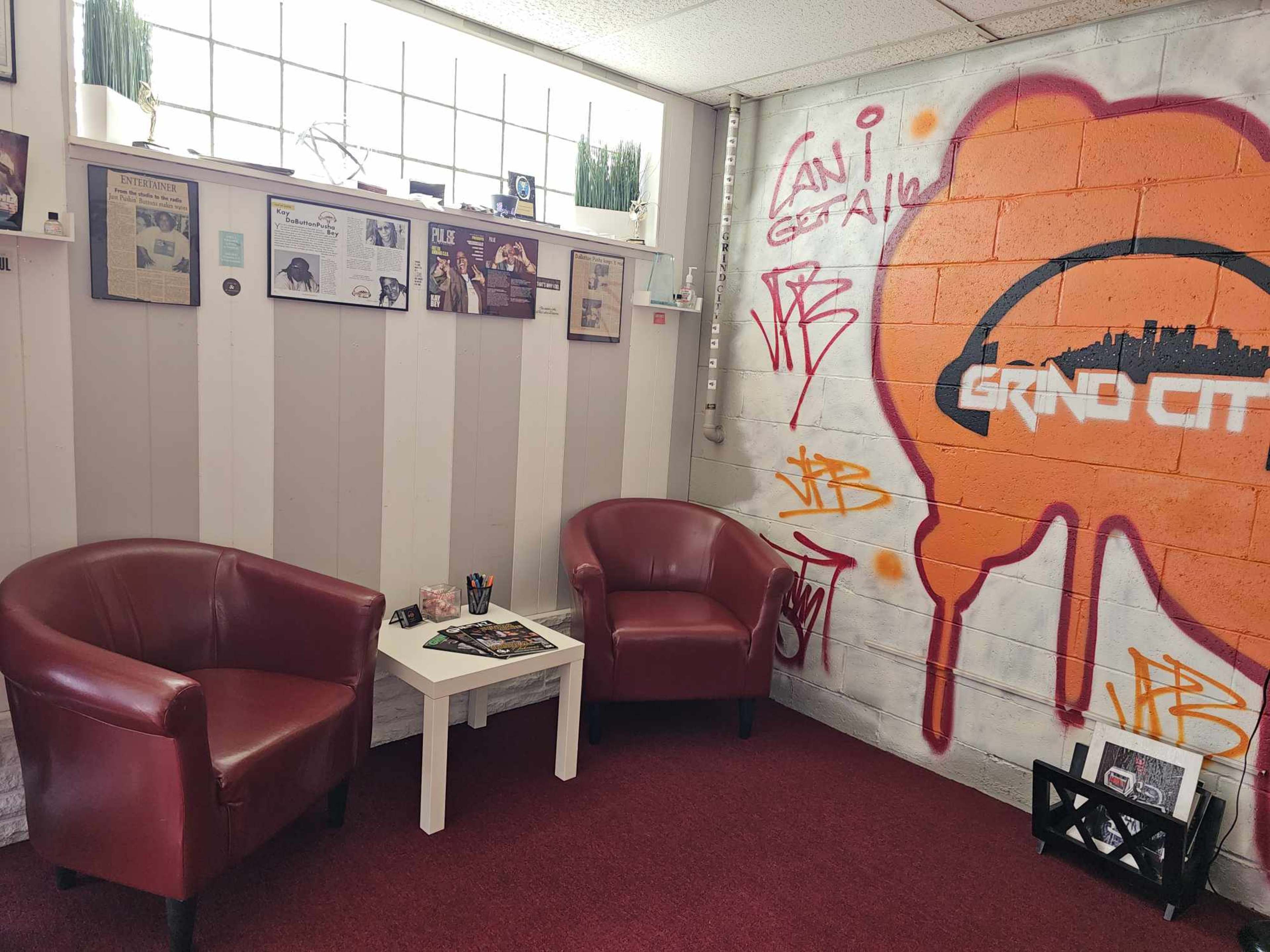 A small waiting area with two red chairs, a white table, and a wall decorated with framed articles and graffiti.