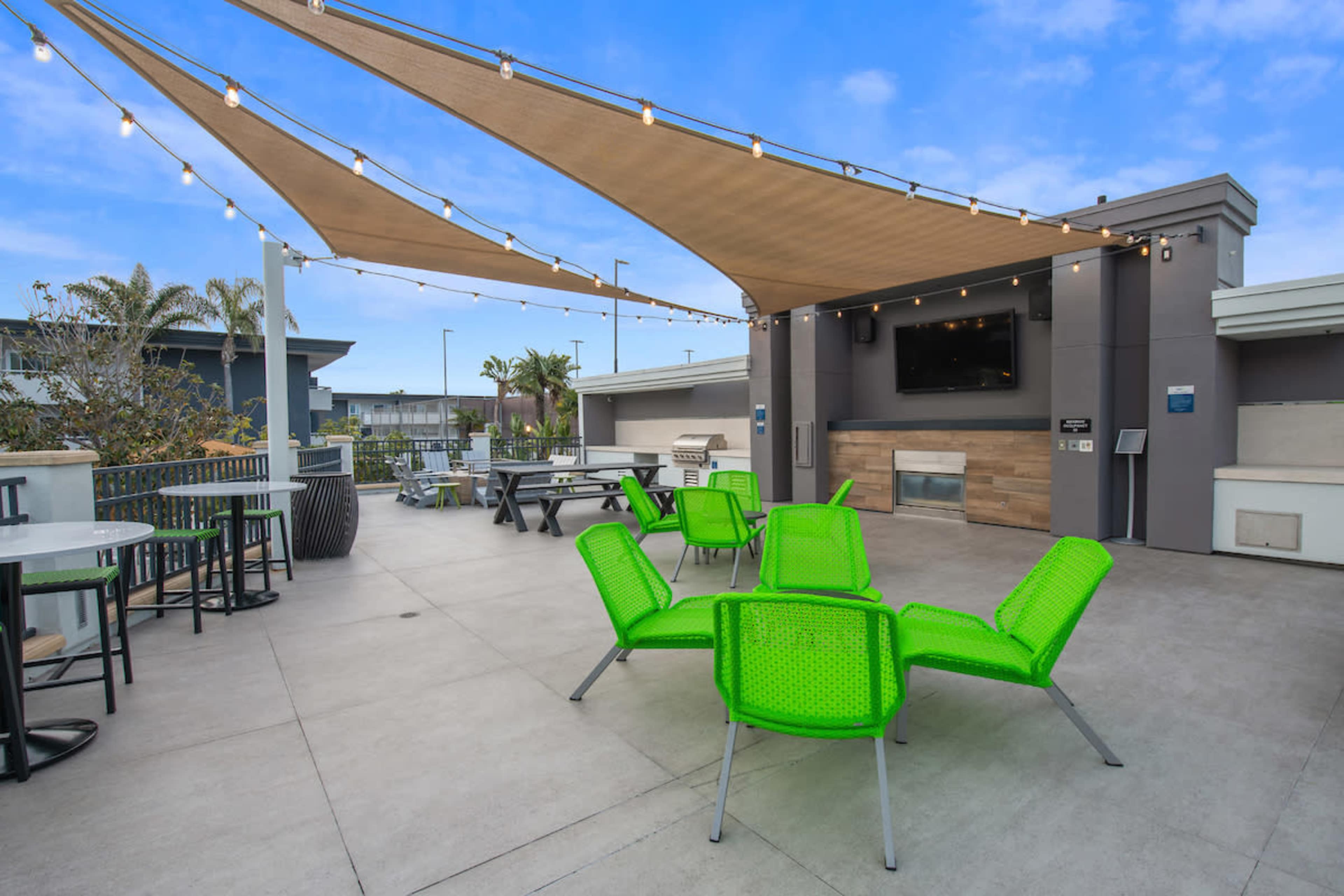 A rooftop terrace features green chairs and tables under a large canopy with string lights.